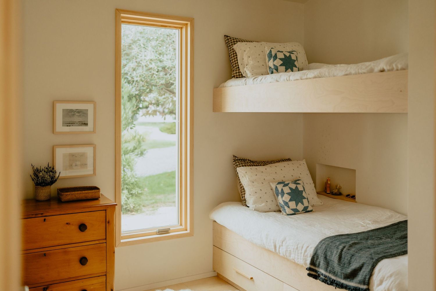 Modern bedroom with bunk beds, wooden dresser, and large window with natural light.