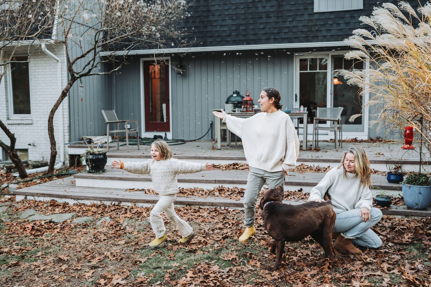 A series of playful outdoor autumn photos with a dog and flowing white dress in front of a grey house.