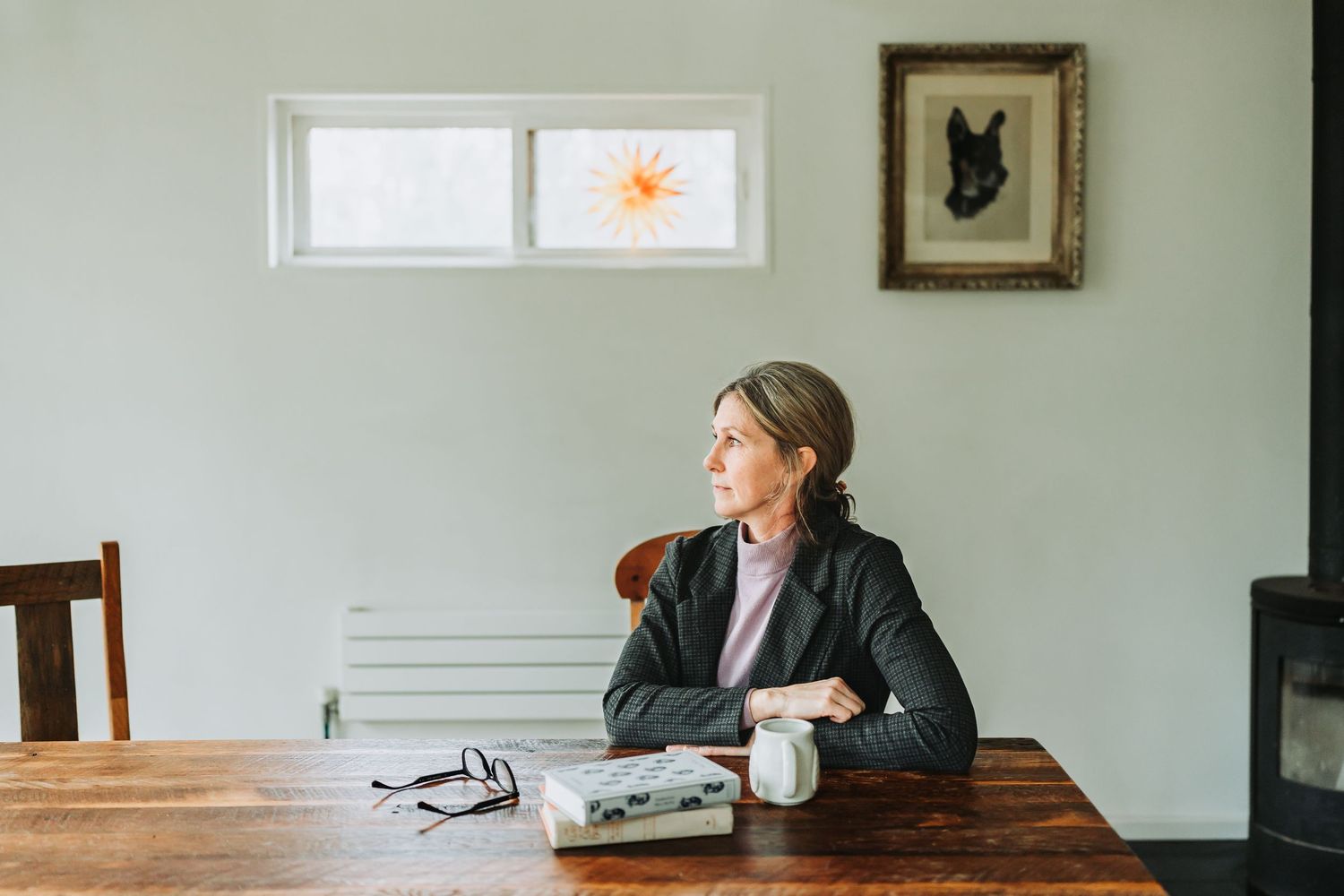 Person in business attire sits contemplatively at wooden table in minimalist room with natural lighting.