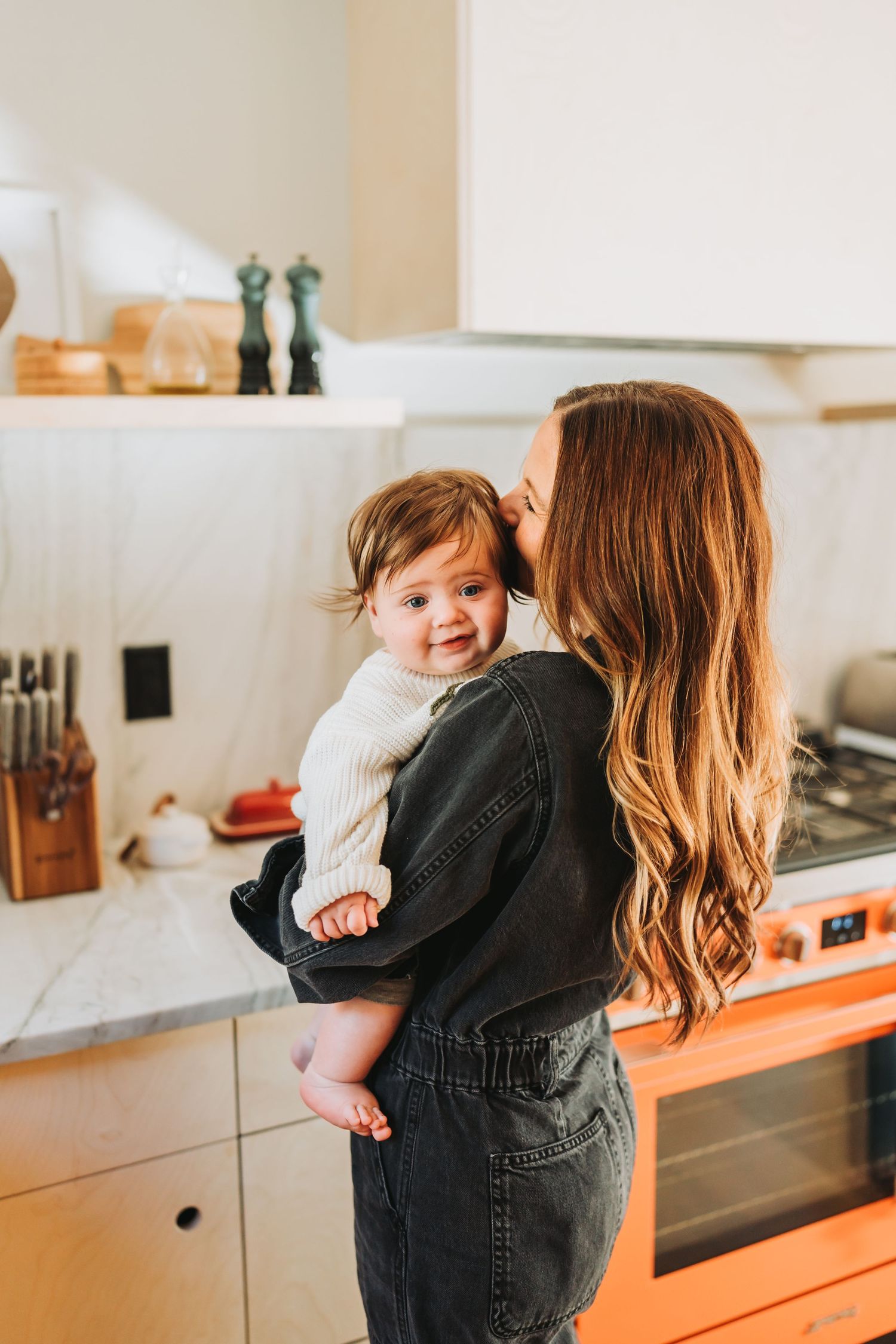 Mother holding young child in modern kitchen with white countertops.