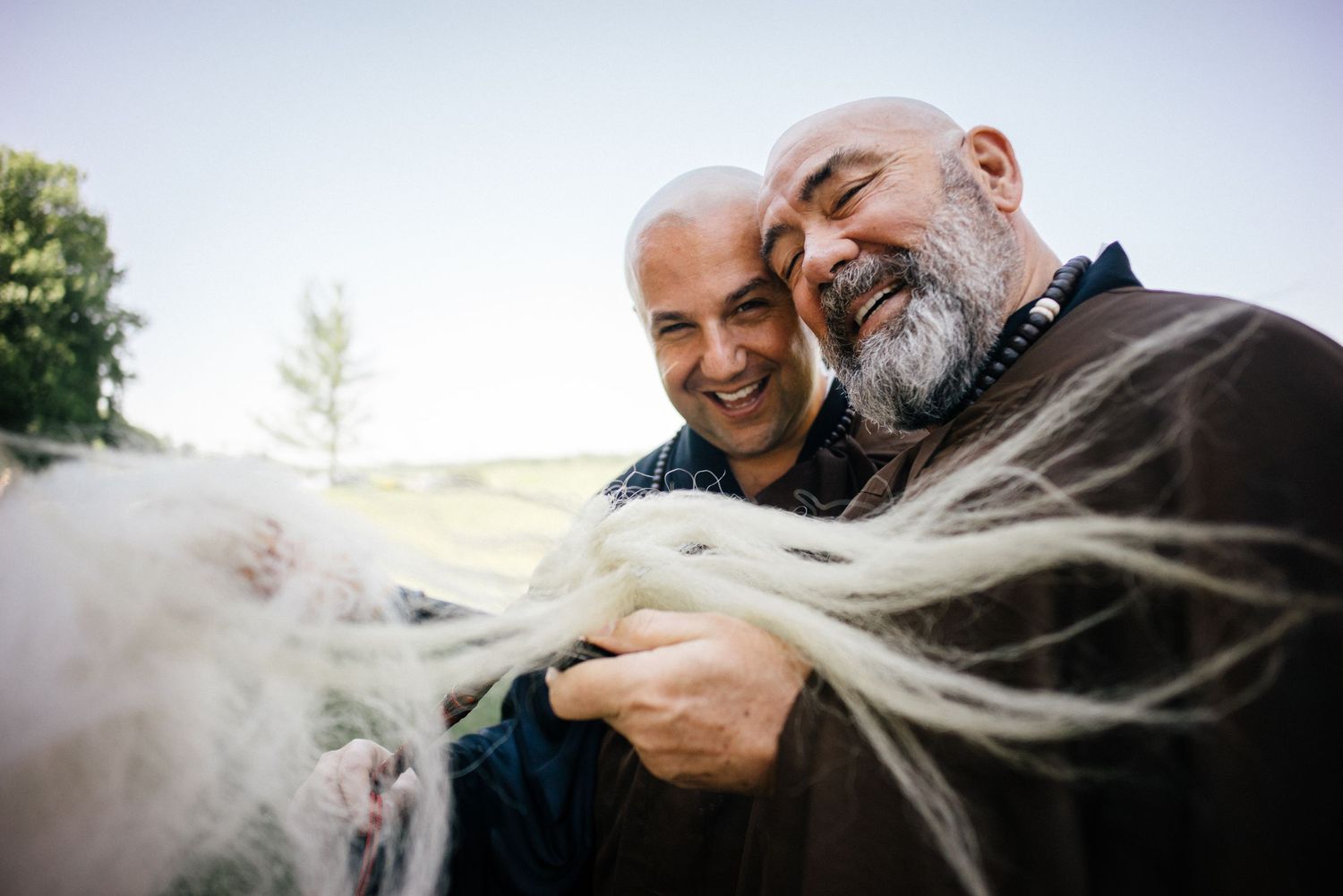 Two men in zen robes sharing a lighthearted moment outdoors on a sunny day.