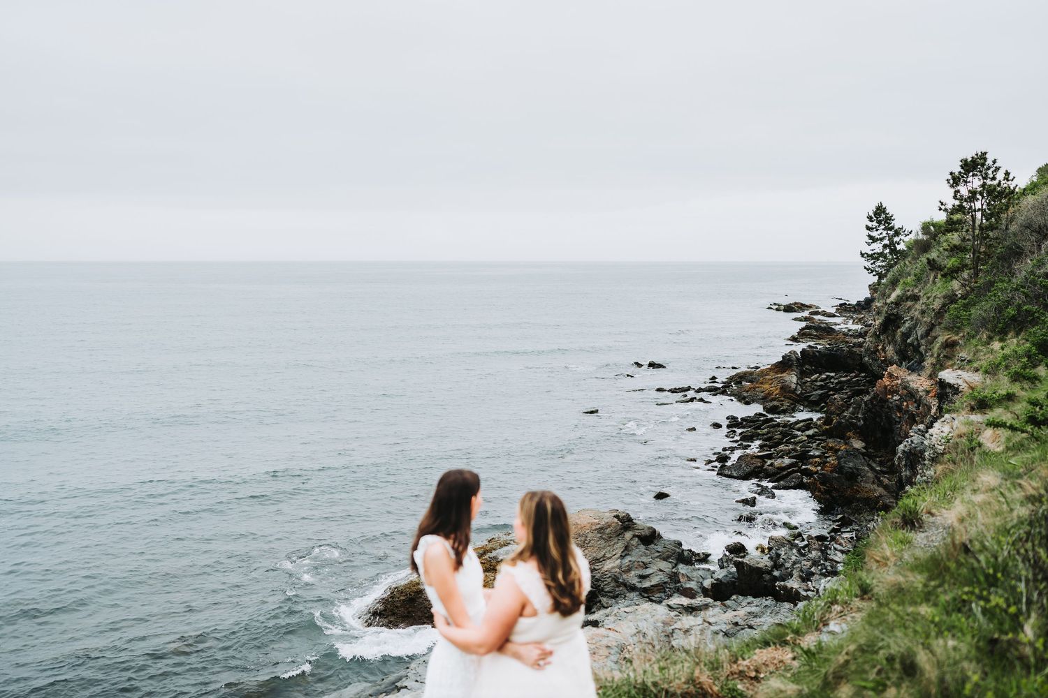 A couple embraces on a rocky cliff overlooking a misty Pacific Northwest coastline during an intimate wedding ceremony.