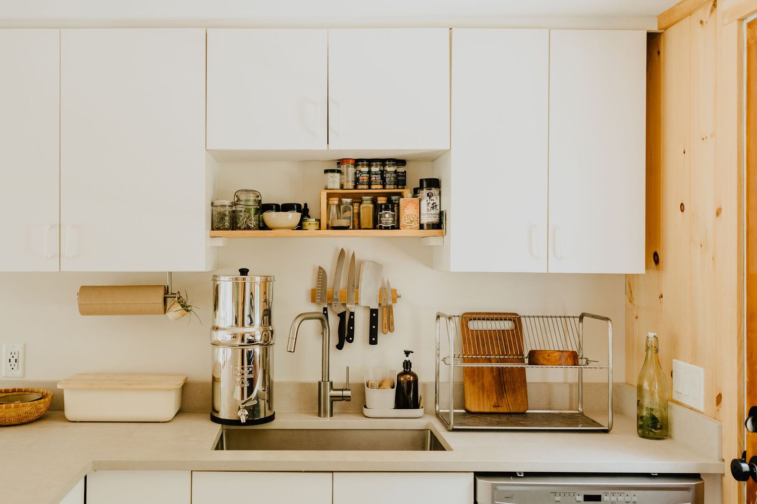 Modern white kitchen interior with wood accents features built-in appliances and floating shelves for a minimalist design.