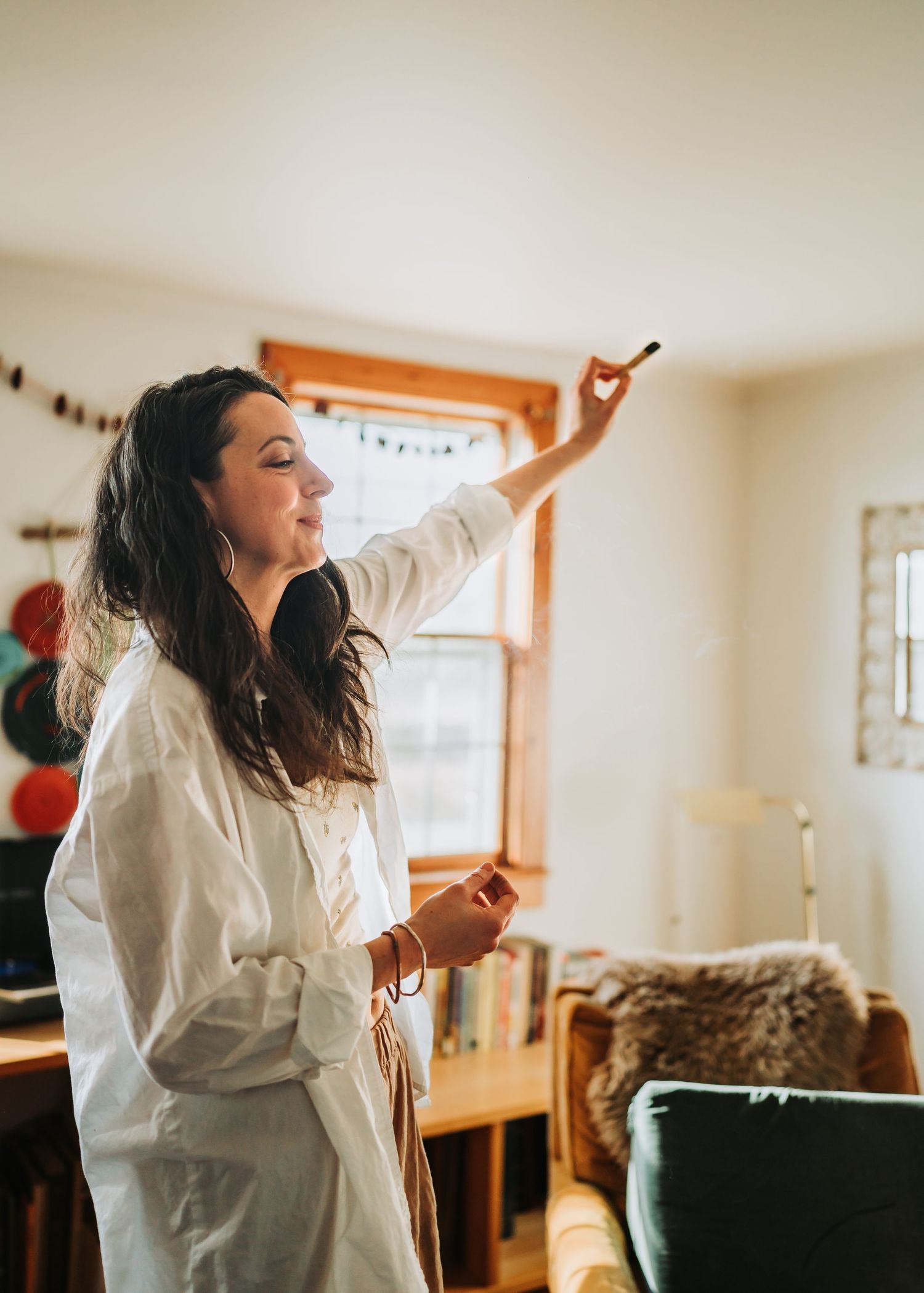 Dancing person in a white shirt moves energetically in sunlit room with string lights and balloons in the background.