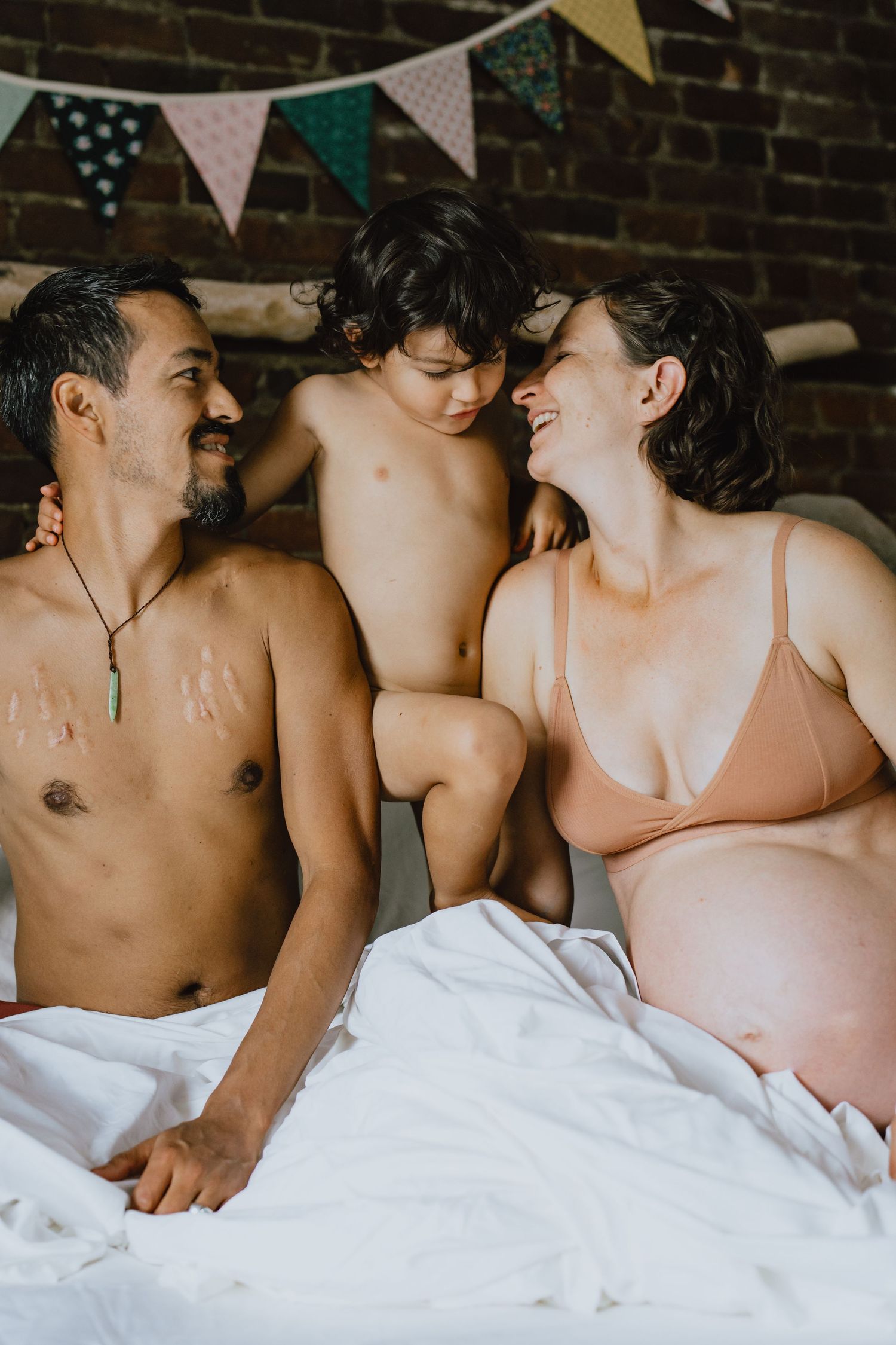 A family sharing joyful moments together on white bedding with decorative bunting overhead.
