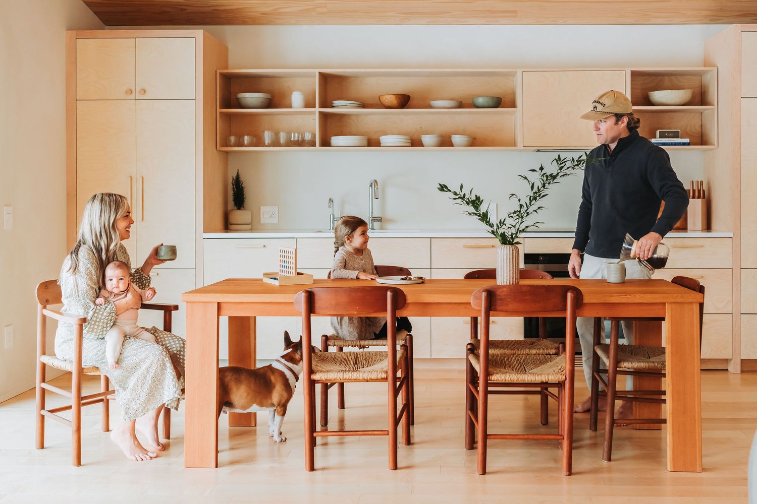 Progressive interior photos show a stylish dining room with wood table, chairs and built-in shelving in warm light.