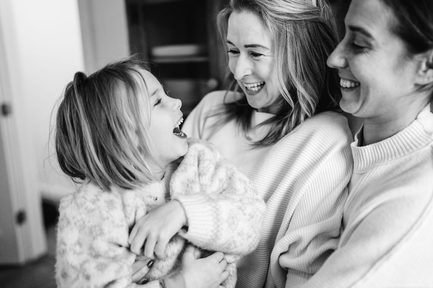 A candid black and white moment of joyful laughter shared between three people in cozy sweaters.