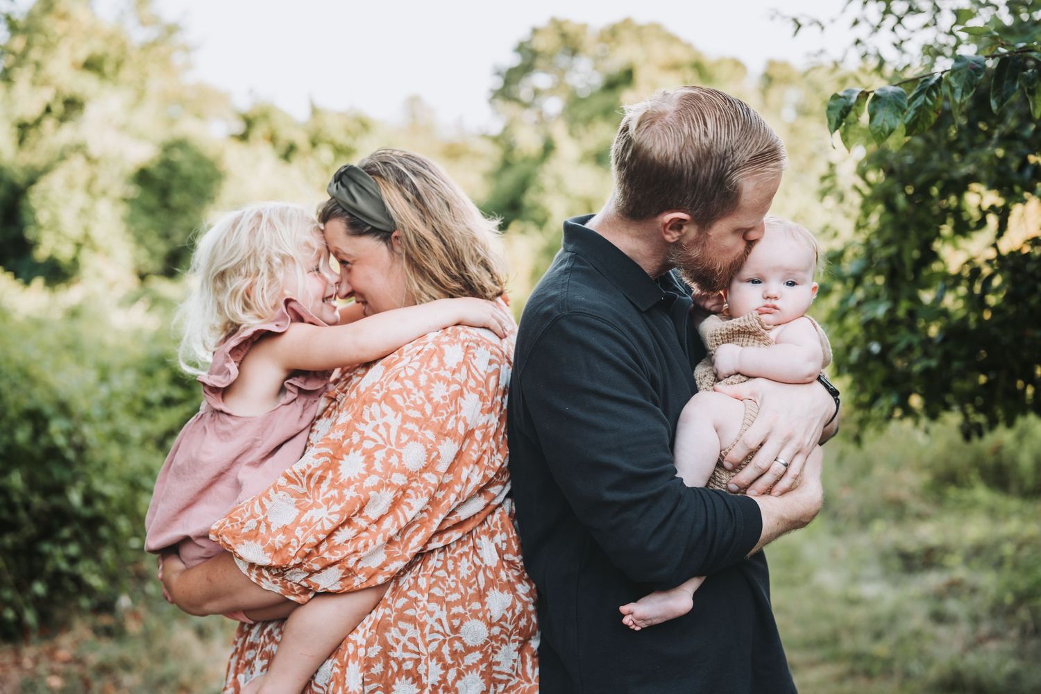 A tender family embrace is captured in sequence outdoors during a sunny afternoon in a lush garden setting.