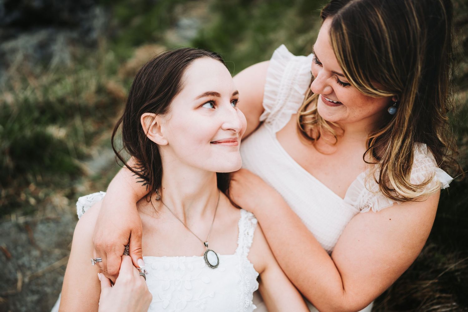 Two women share tender moments in an outdoor photoshoot with warm natural lighting.
