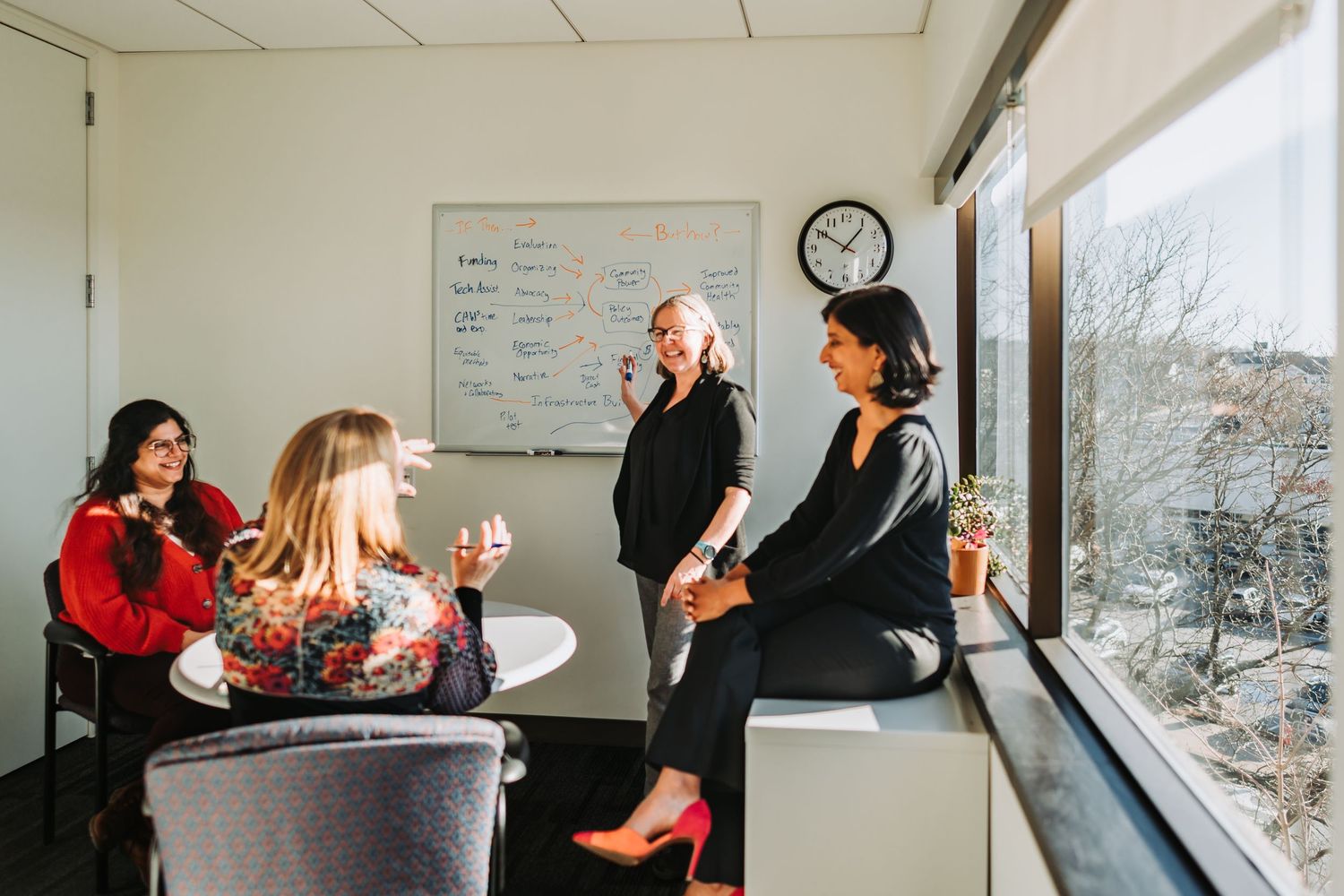 People gather in an office space for a casual meeting while enjoying drinks and conversation.