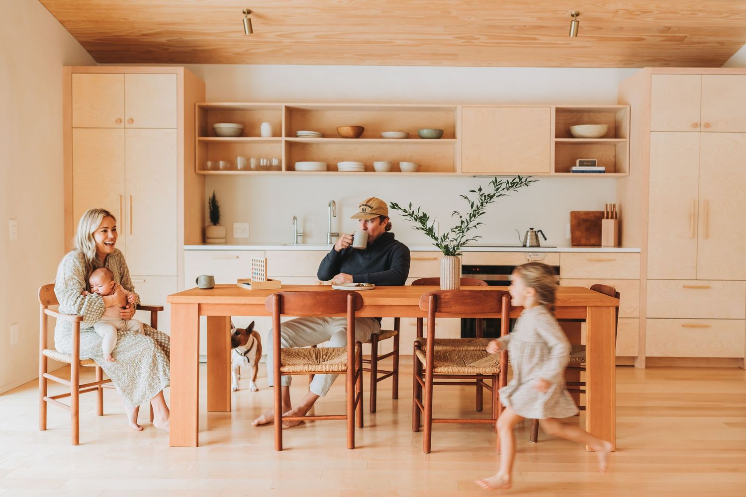 Panoramic view of a minimalist kitchen with light wood cabinets and dining furniture.