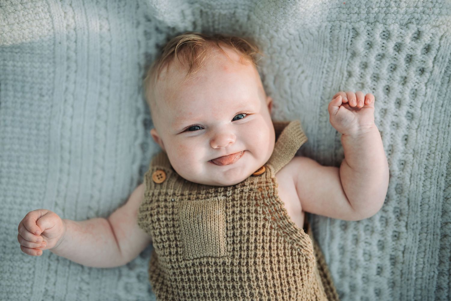 Baby wearing beige knit outfit lying on textured blue blanket.