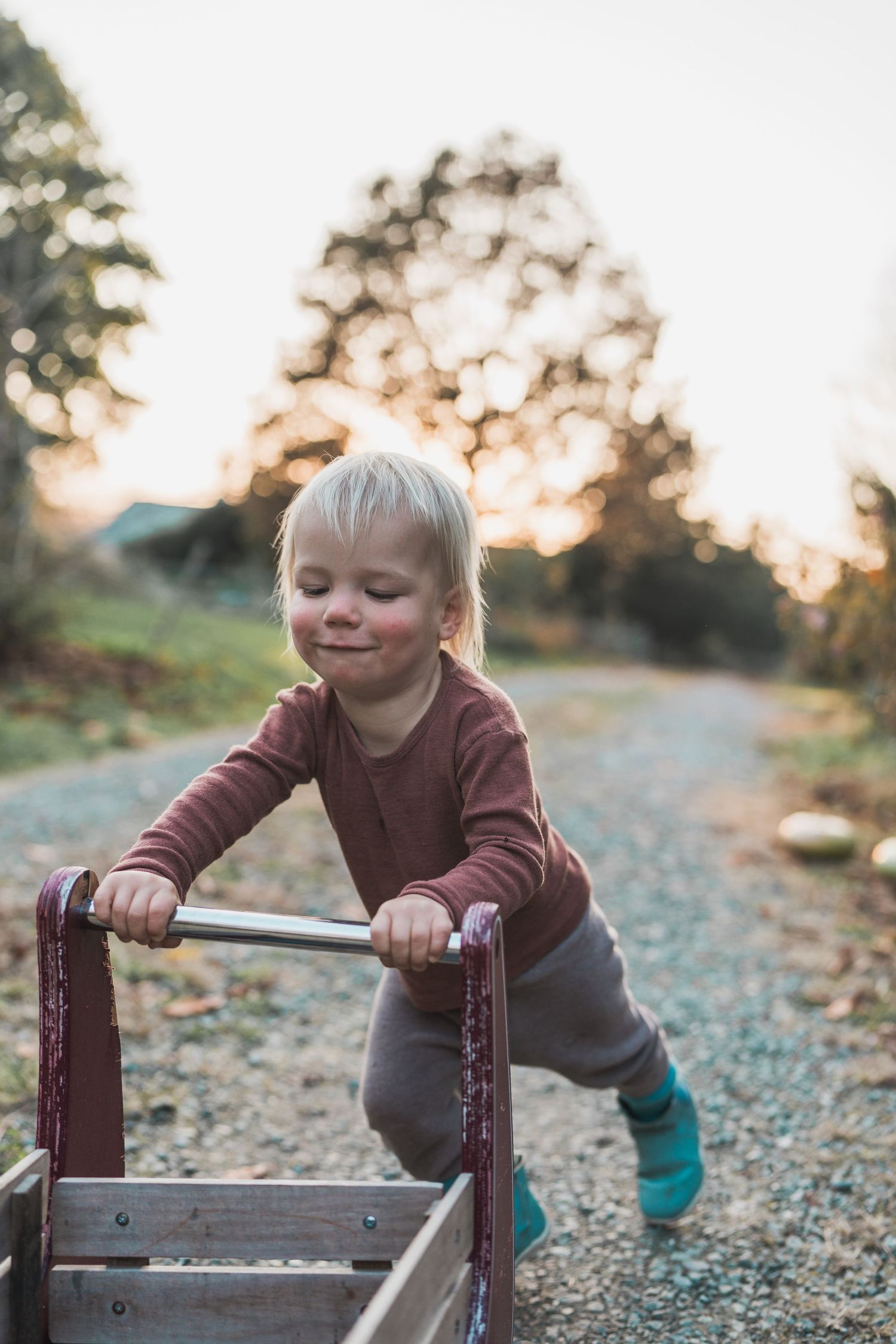 Young child playing with a wooden wagon on a gravel path at sunset.