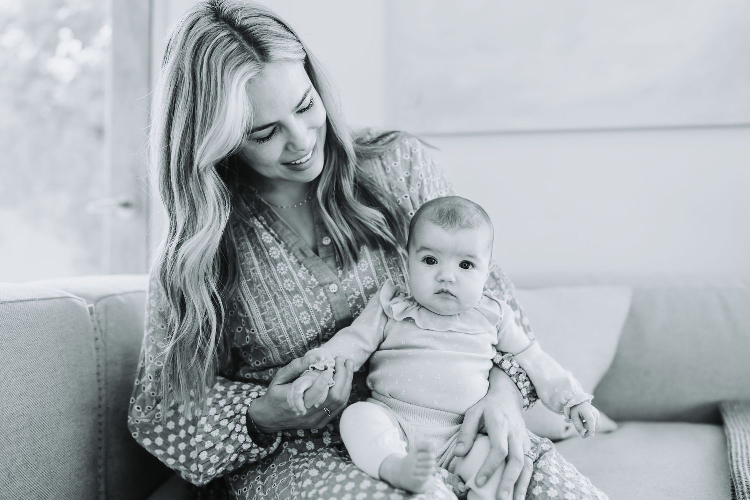 Parent and baby share tender moments on a sofa in a series of cozy black and white photographs.