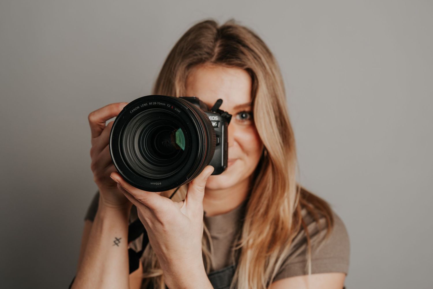 Professional photographer captures photo with large DSLR camera against grey background.