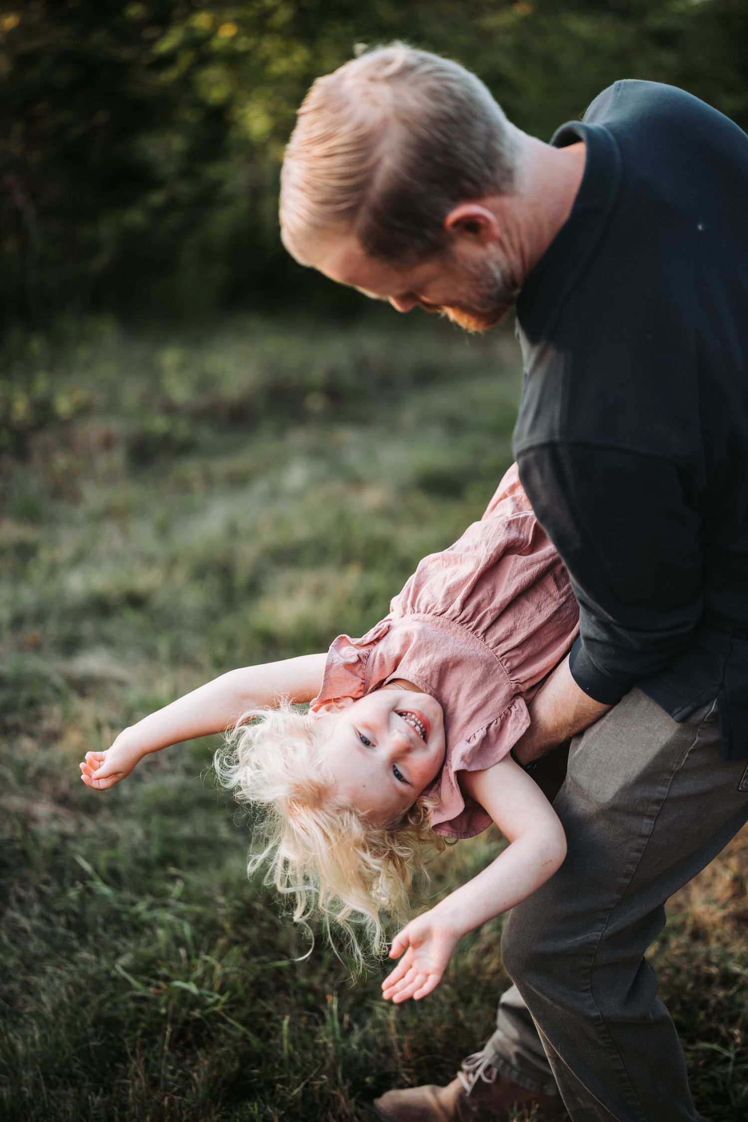 Playful scene of parent swinging child through the air in a grassy outdoor setting at golden hour.