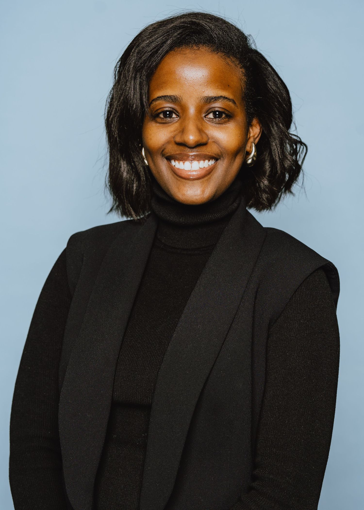 Professional headshot series showing someone in a black turtleneck and blazer expressing different emotions against a blue background.
