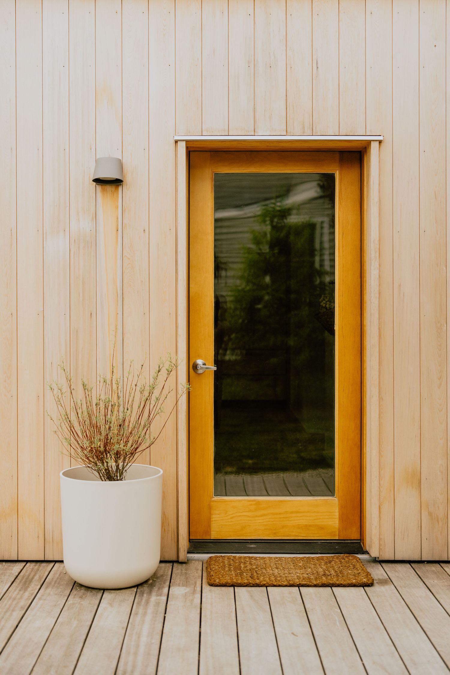 Yellow glass door with white planter and natural wood siding creates welcoming entrance.