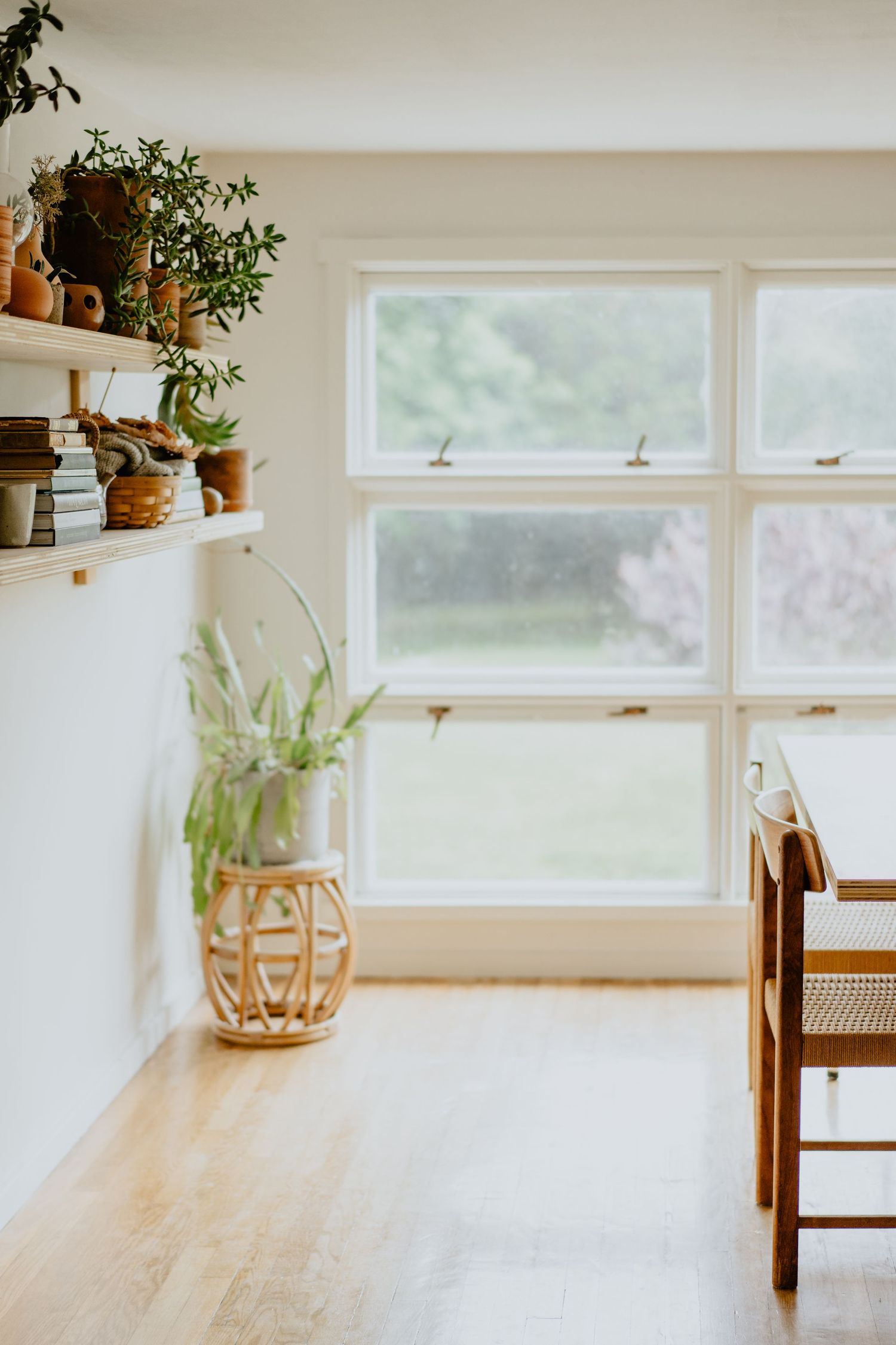 Minimalist dining room interior with wooden table, window view and potted plants on floating shelves.