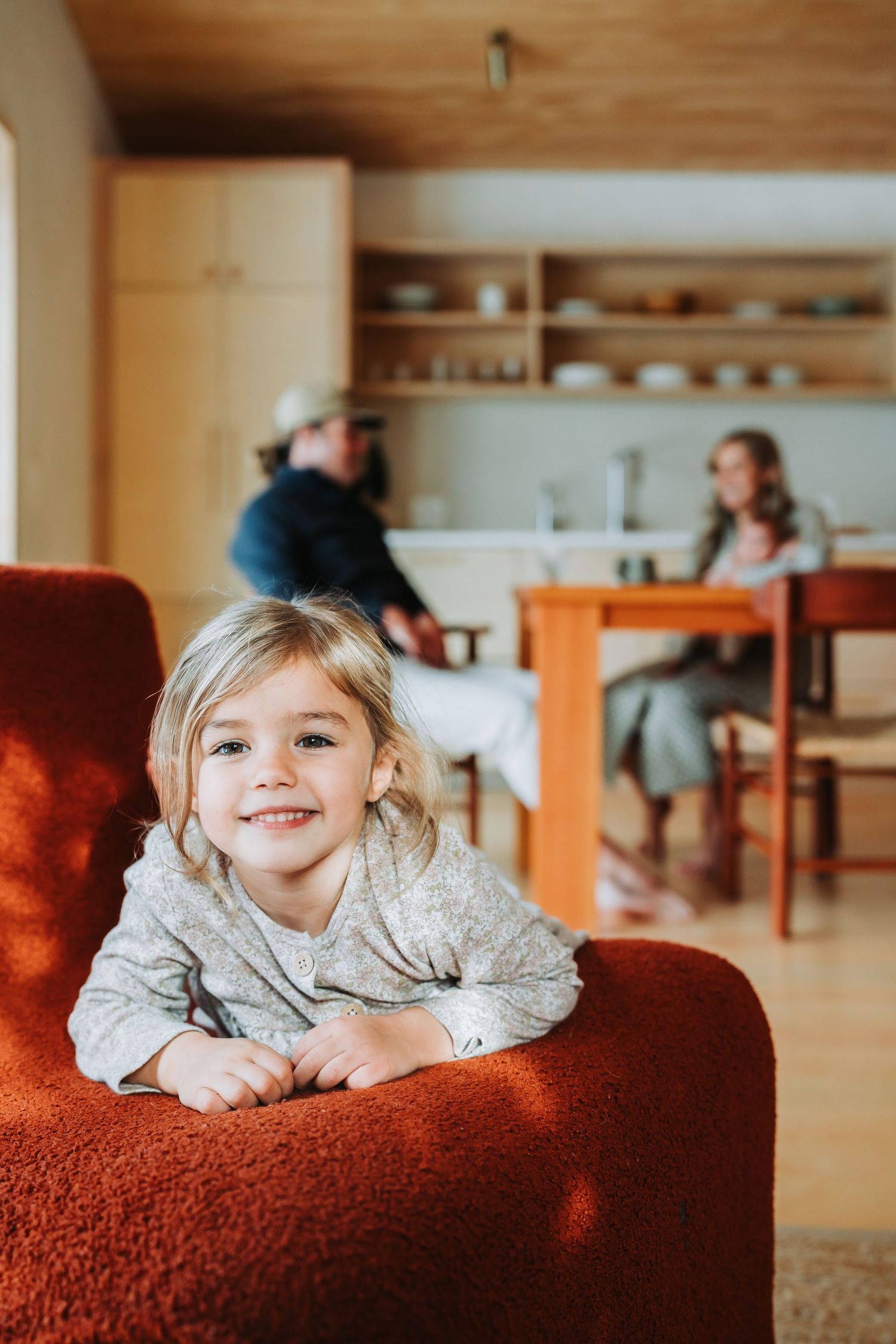 Three consecutive photos show a young child lying on a cozy red couch in a warm, wood-paneled interior space.
