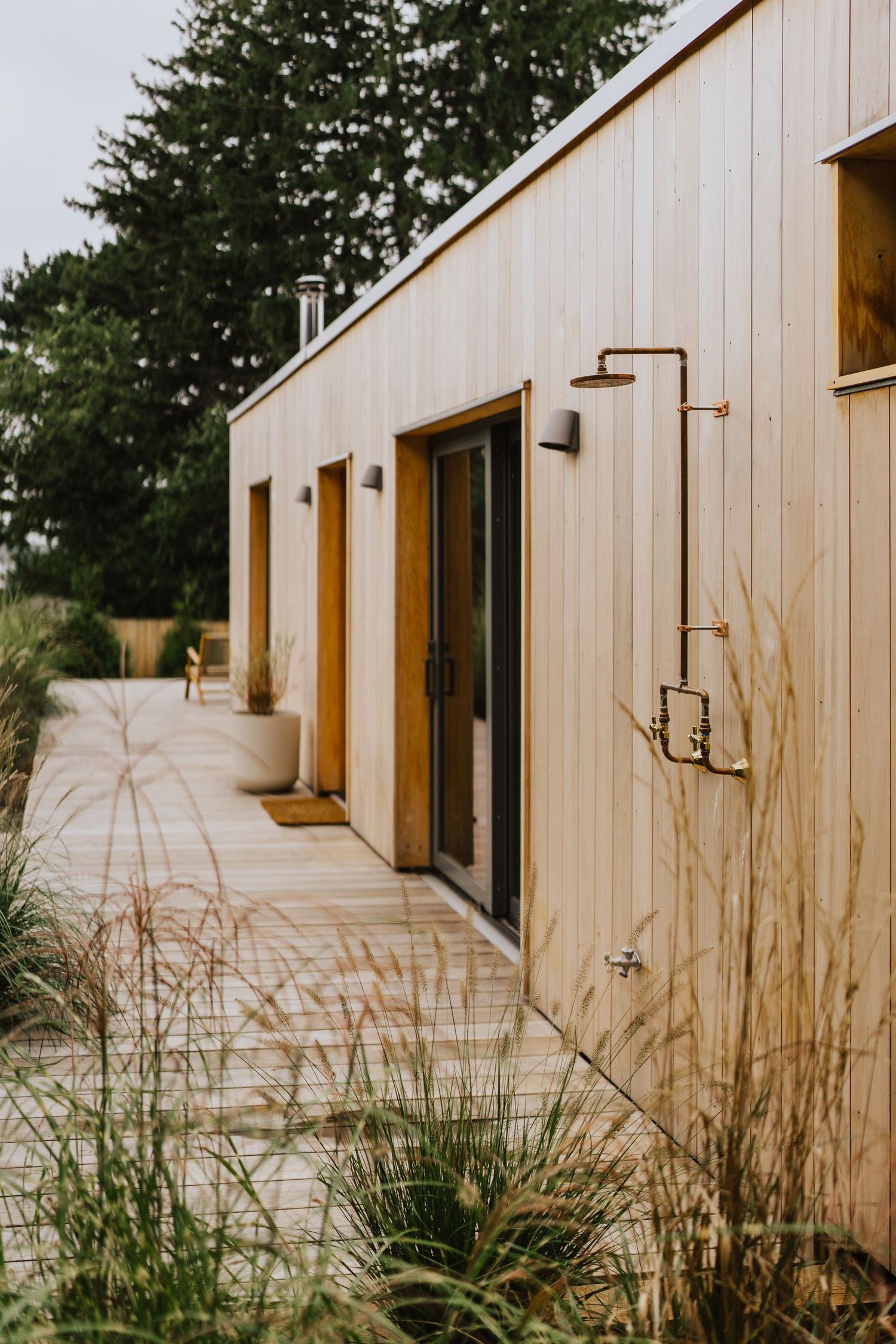 Modern wooden building exterior with sliding glass doors and outdoor shower fixtures.