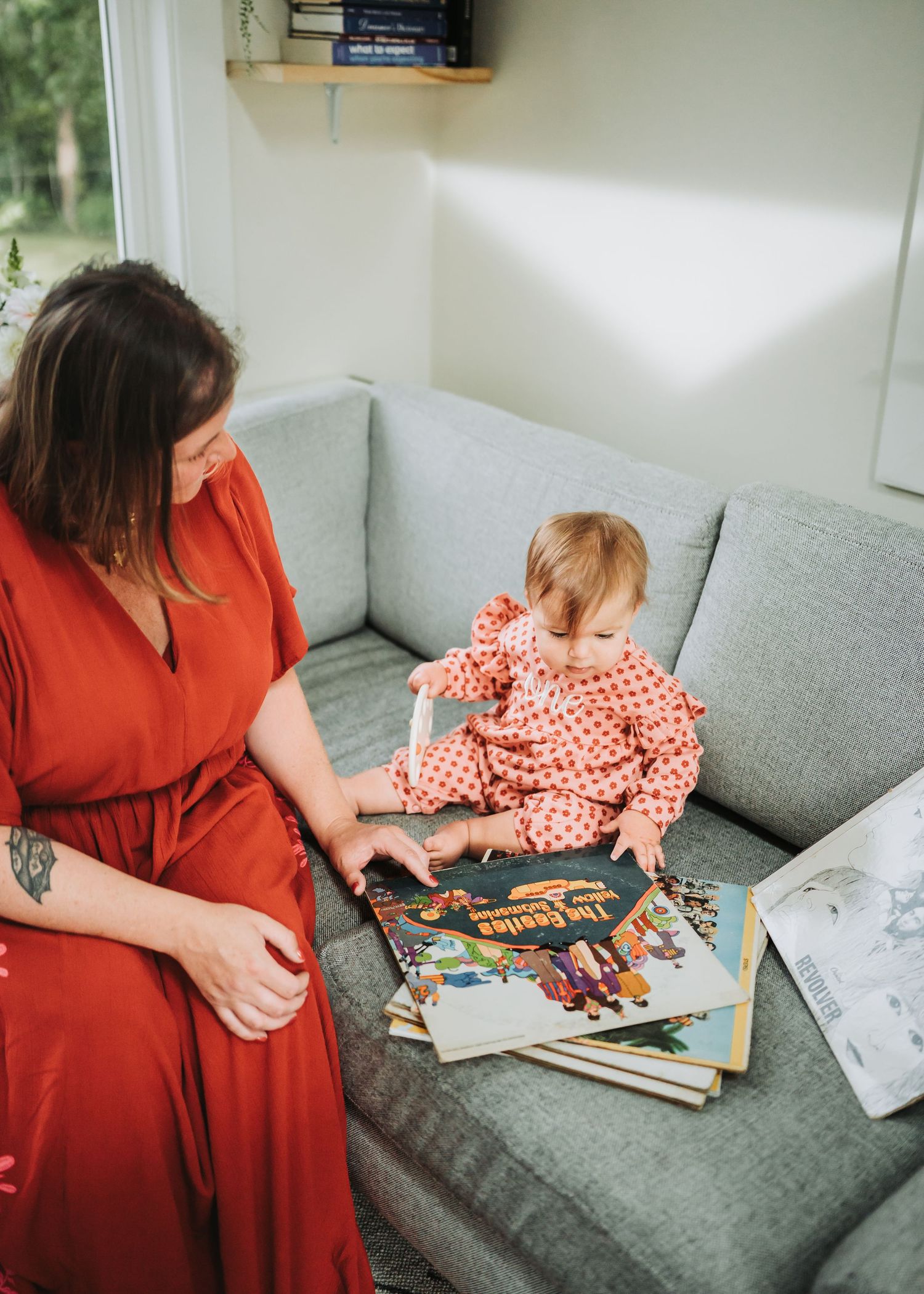 A family reads together on a cozy gray couch, with a parent in red dress sharing a book with a child in polka dots.