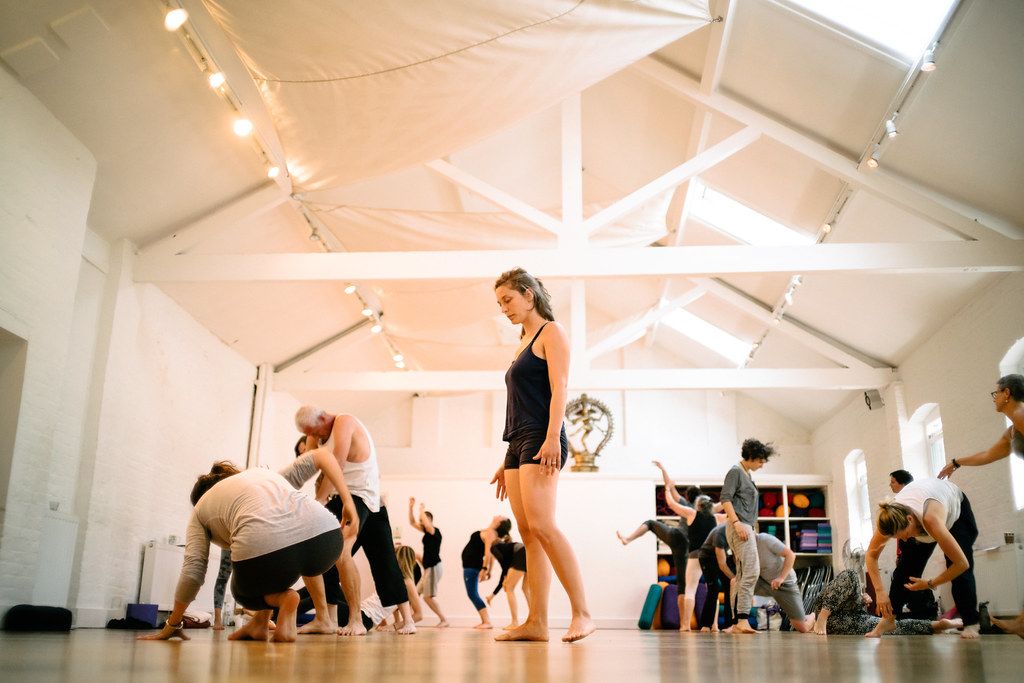 A large group of dancers practicing in a bright white dance studio with string lights decorating the ceiling.