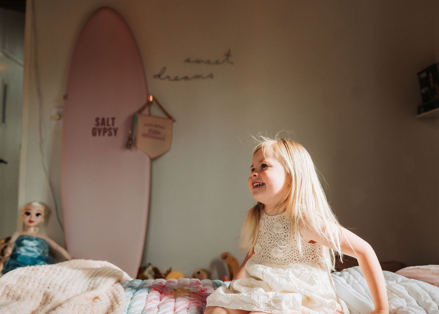 A happy blonde girl bounces on a bed in a surf-themed bedroom with sweet dreams wall decor.