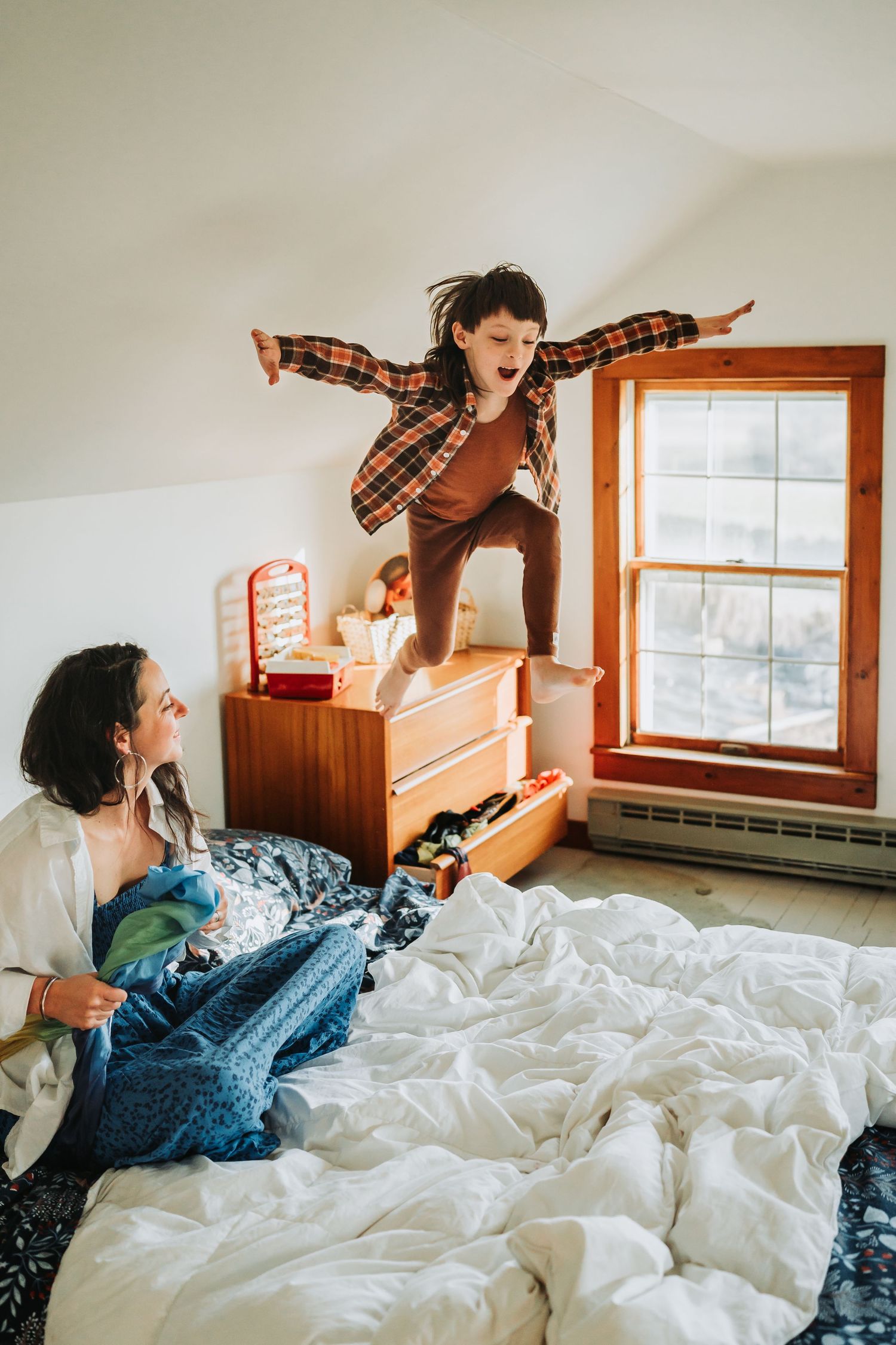 Playful candid photo sequence showing someone lounging and jumping around on rumpled white bedding with morning sunlight.
