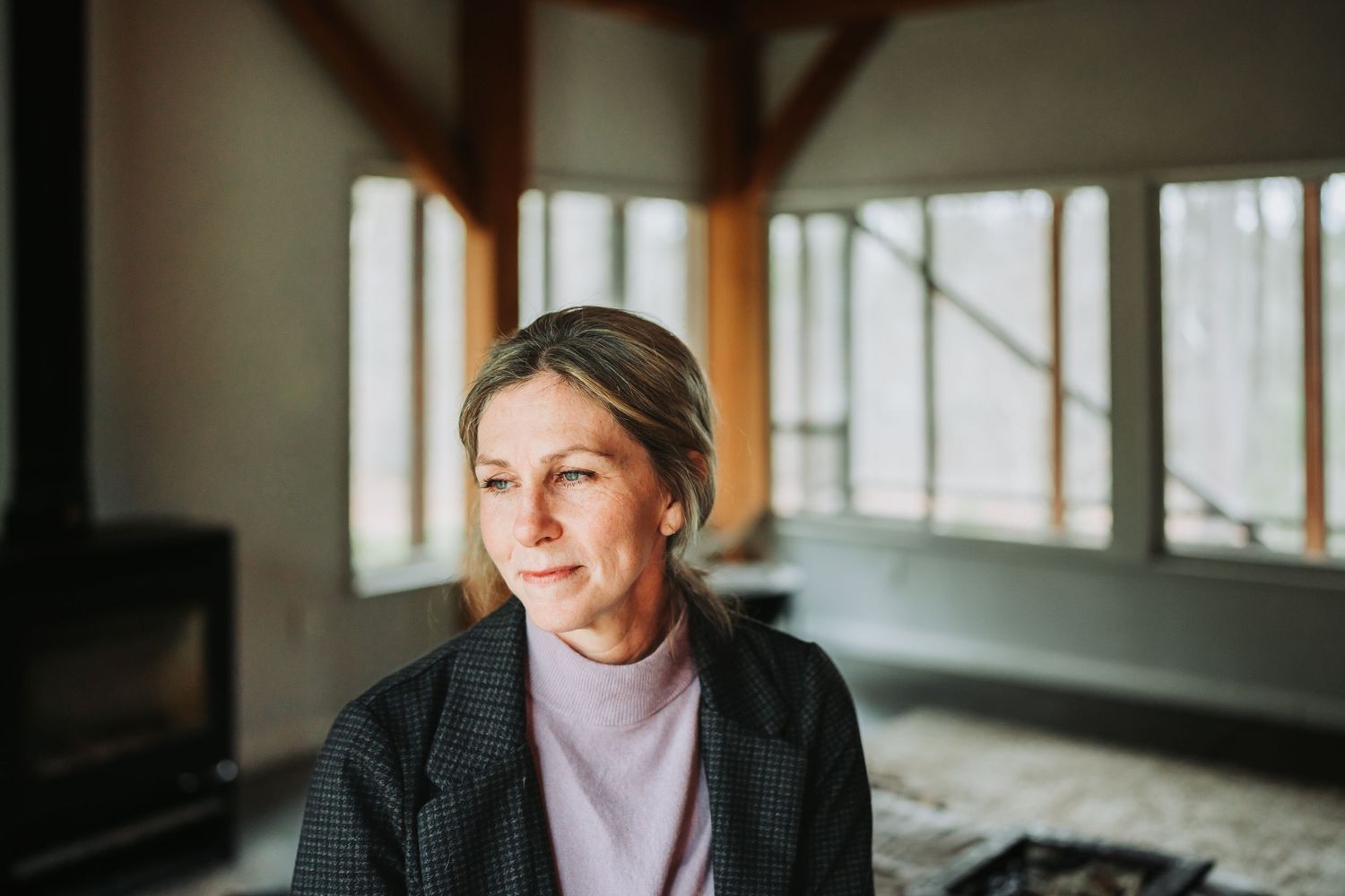 Woman in pink sweater sits by window ledge in natural light interior setting.