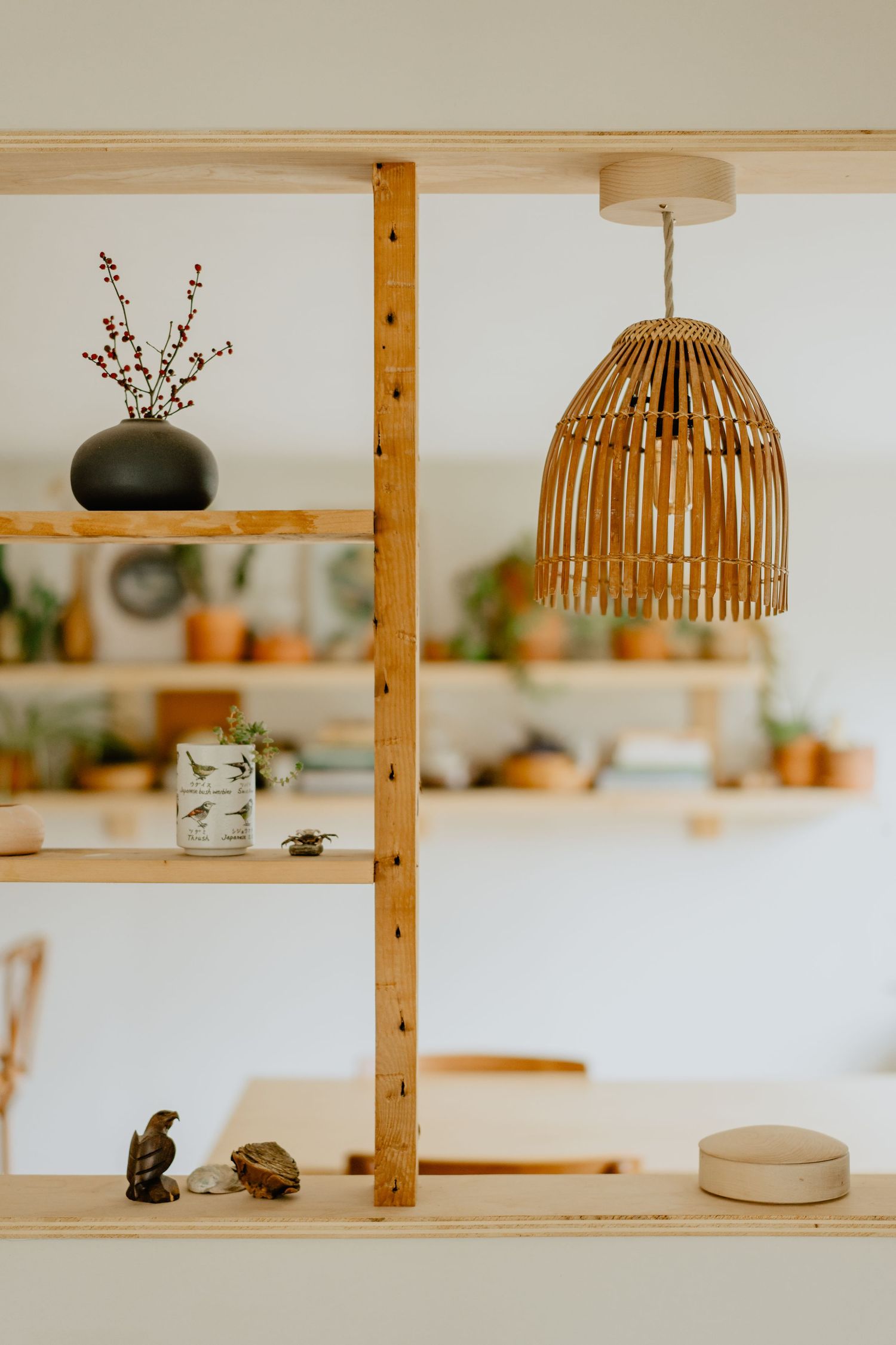 Modern wooden shelving unit displaying decorative items and pendant lamps with natural woven shades.