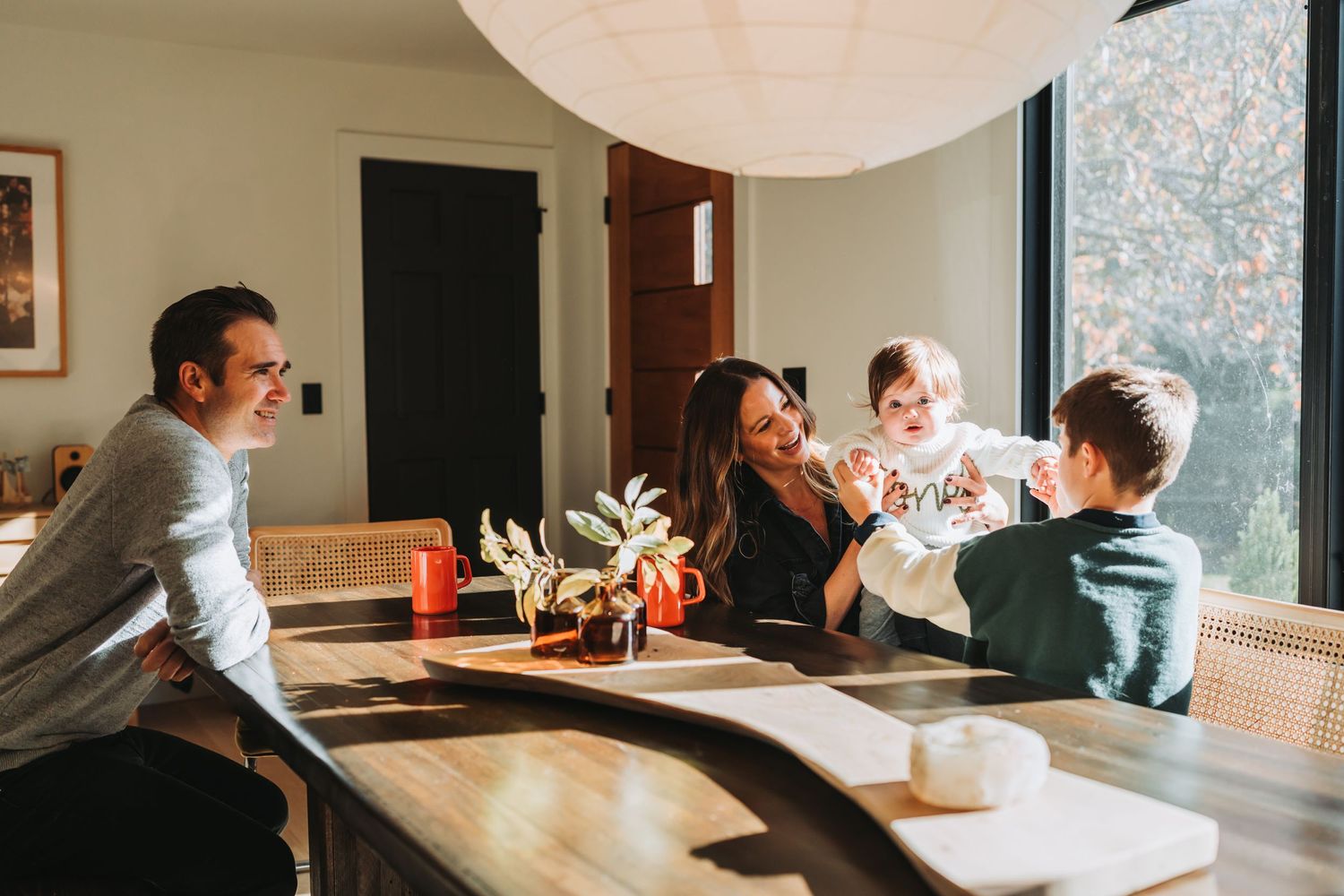 Family gathering around dining table with large windows and natural light.