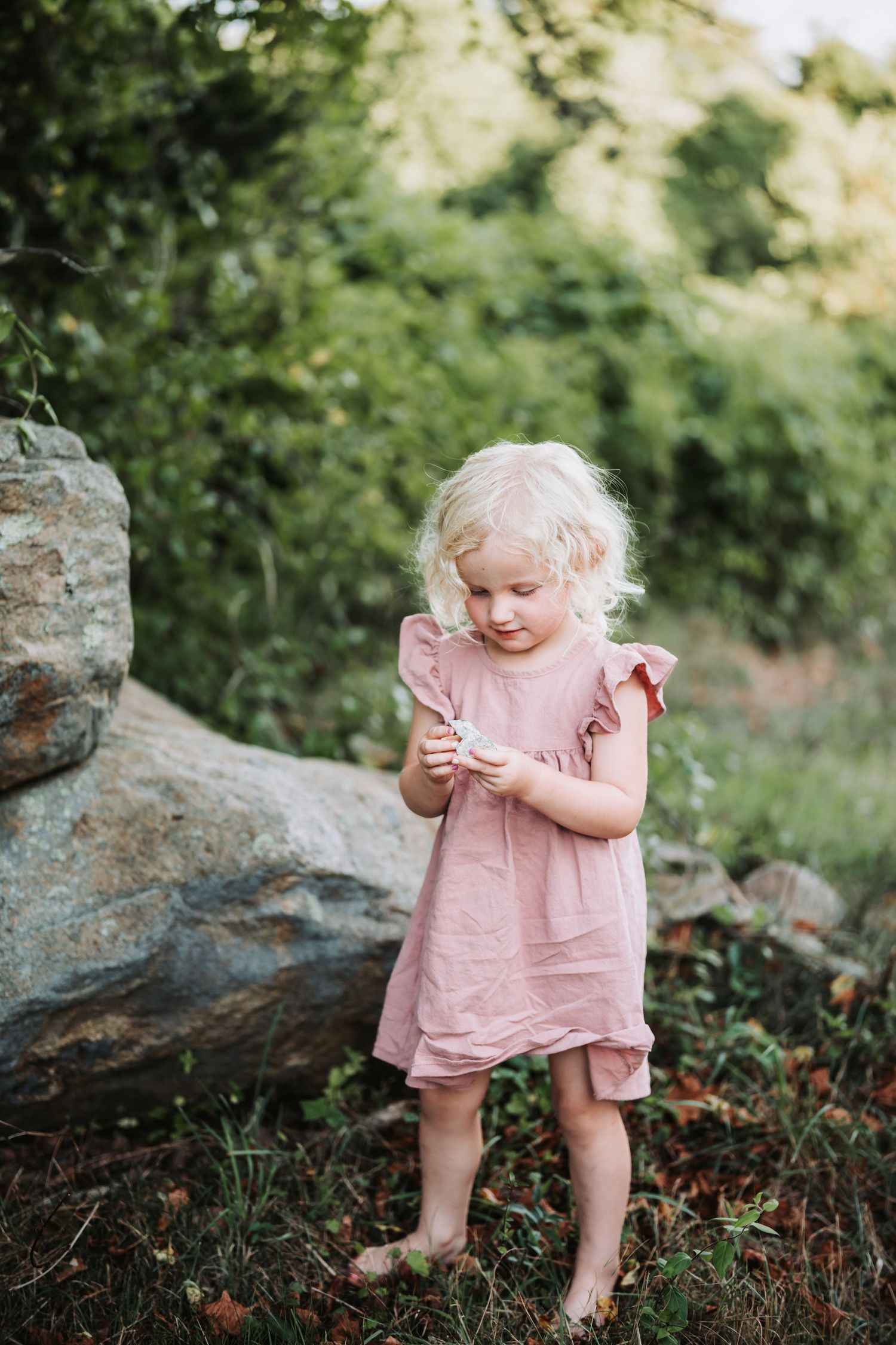 Delightful moment of a small child in a pink dress playing and exploring in a garden setting with rocks and greenery.