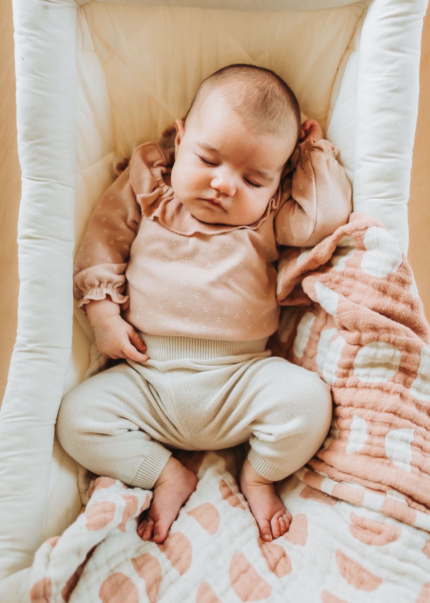 Sleeping infant lying on tie-dye pattern blanket in soft beige and peach colors.
