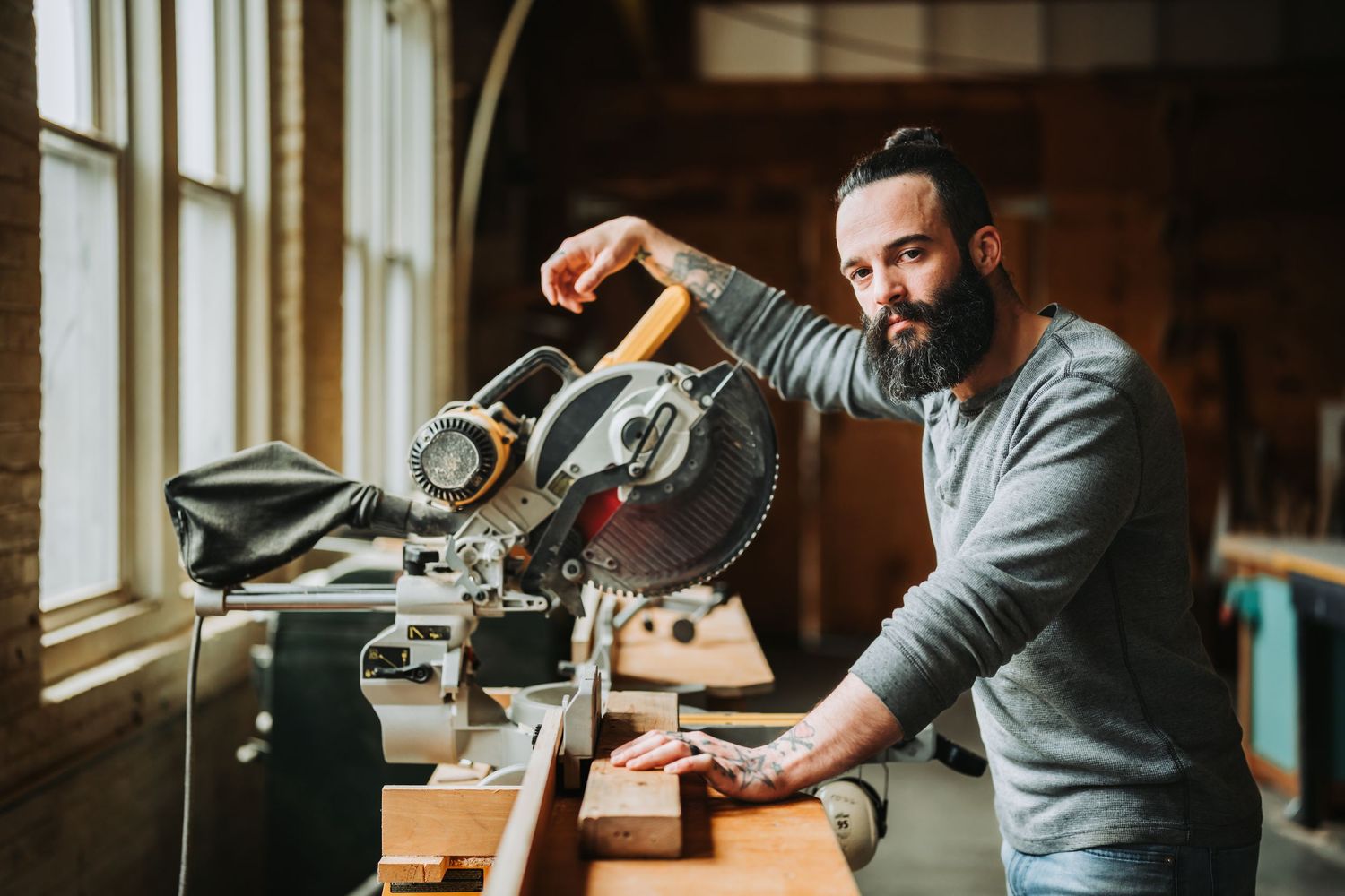 Craftsman working at wooden desk with vintage tools and natural light streaming through workshop windows.