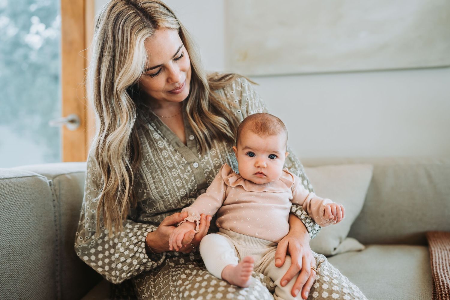 Parent and infant sharing tender moments on grey couch in natural lighting.