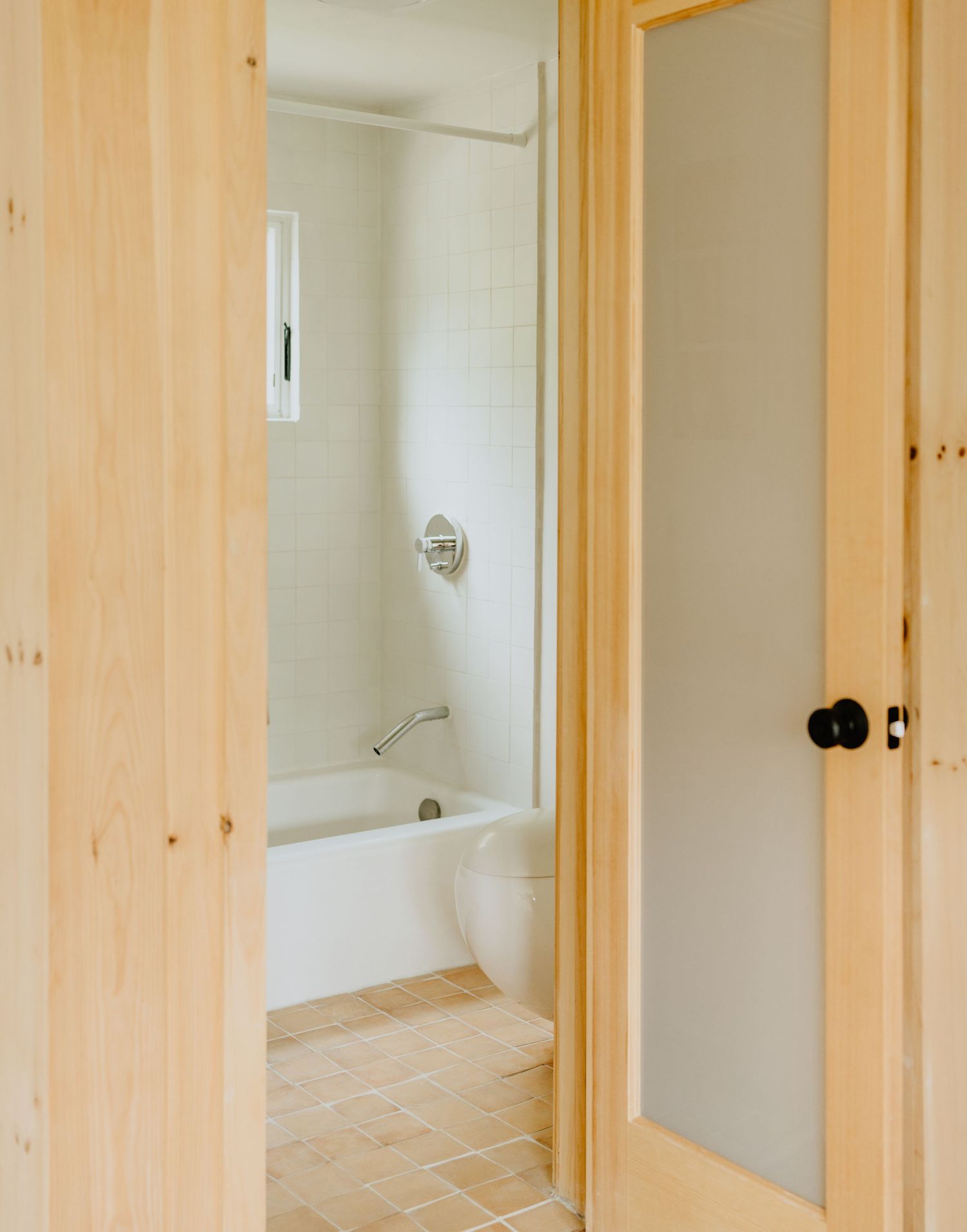 Interior view of a hallway with light pine wood trim and doorframes against white walls and beige tile flooring.