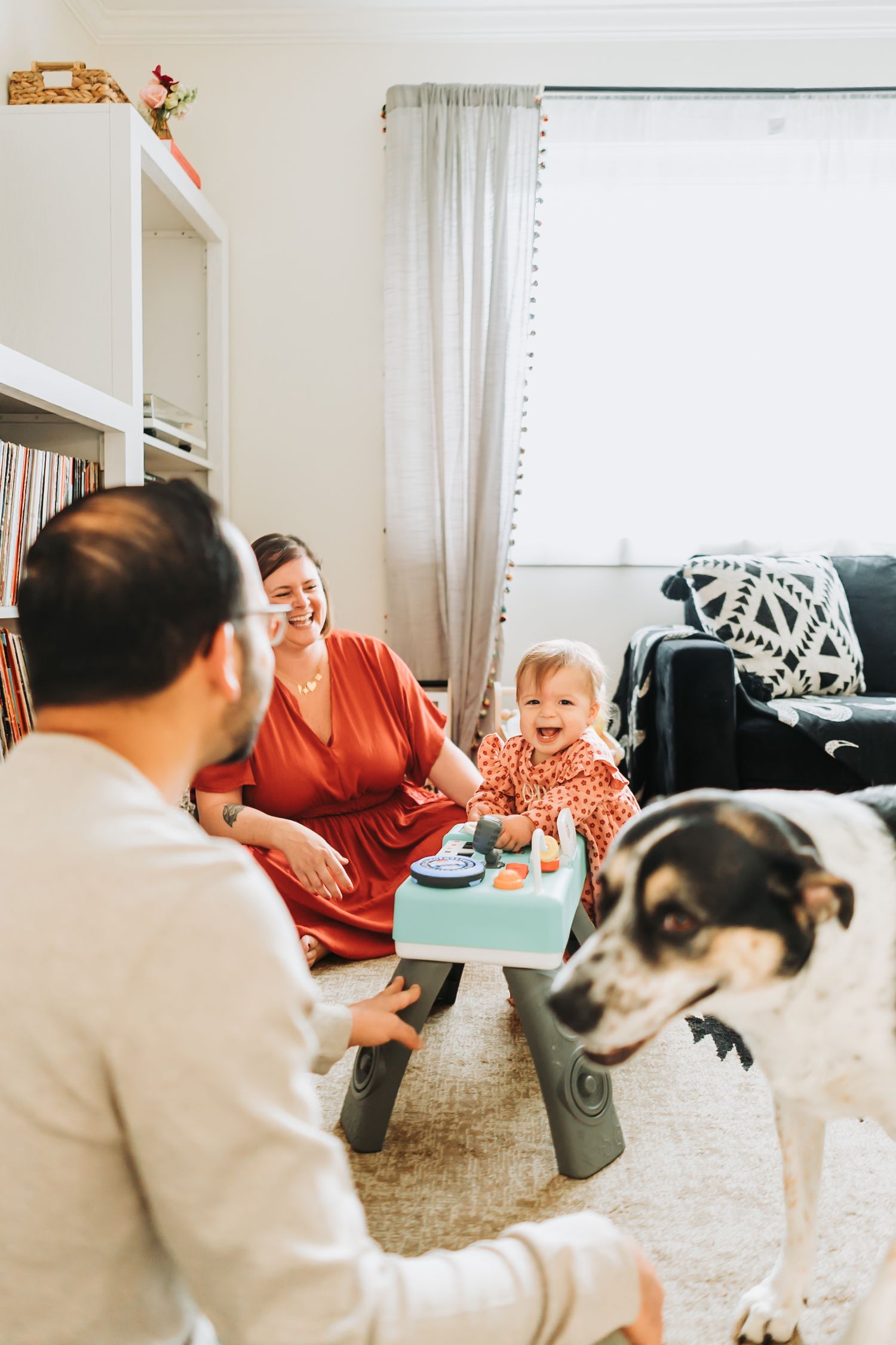 A family relaxes on the living room floor while playing with their black and white dog.