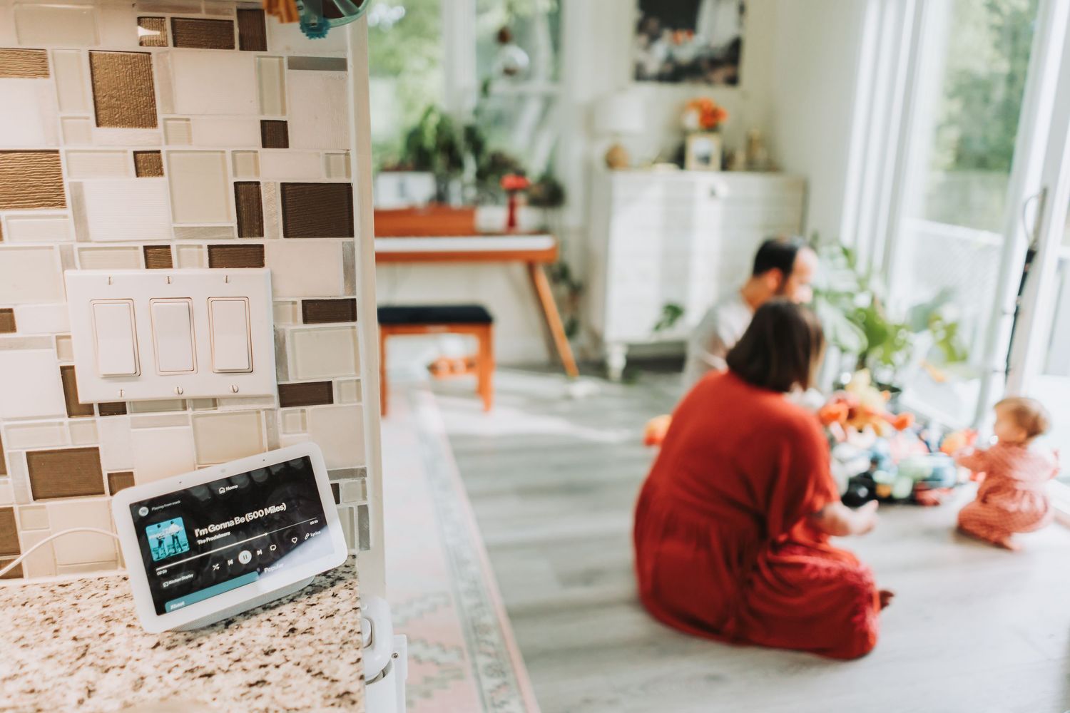 A cozy home interior with a wall-mounted thermostat and people sitting on the floor in red clothing.