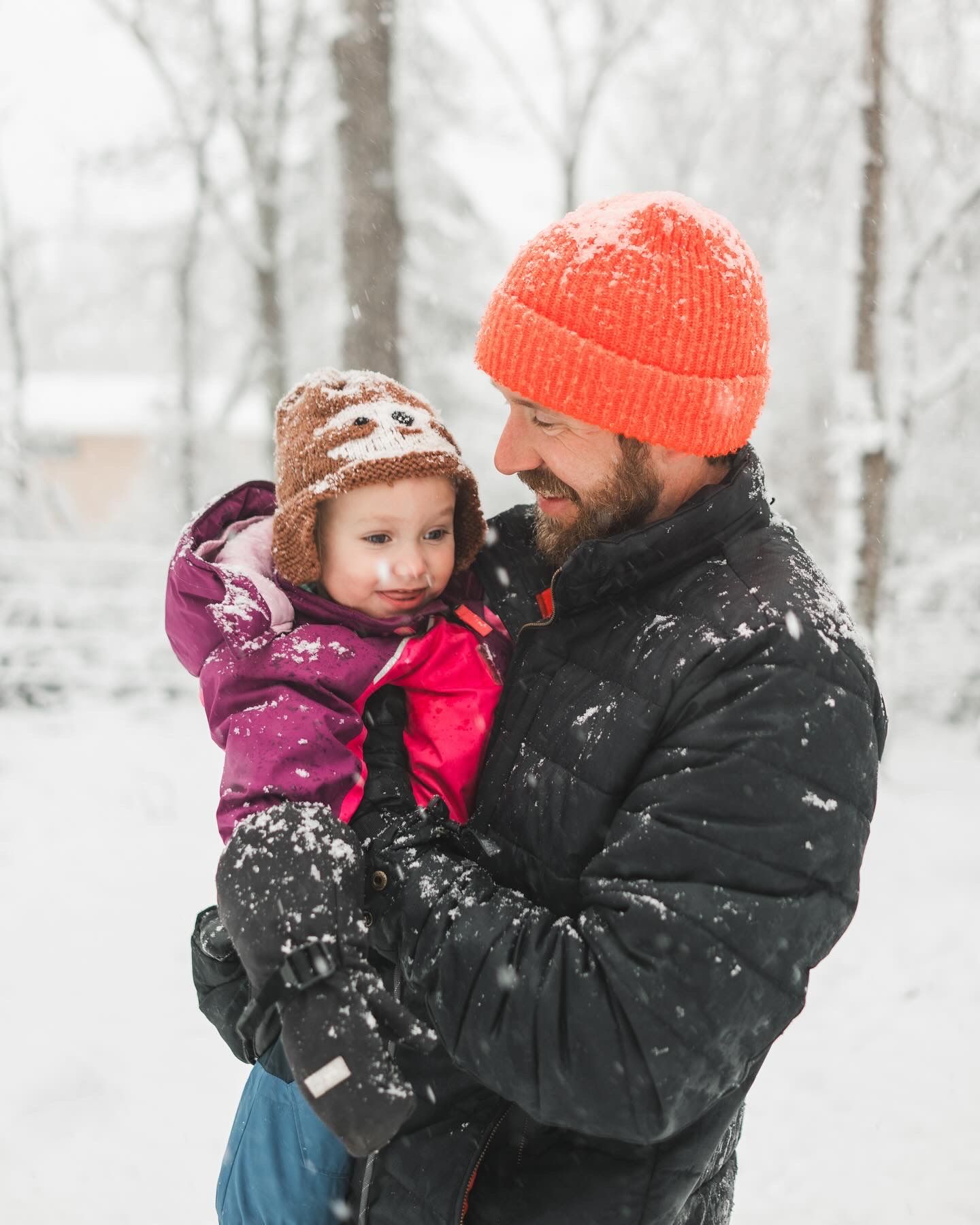 Winter scene with father and child in warm clothing and falling snow.