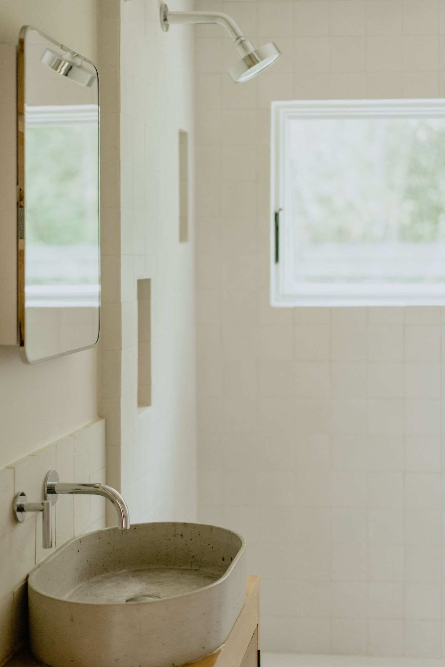 Contemporary bathroom featuring a concrete vessel sink, frameless mirror, and window letting in natural light.
