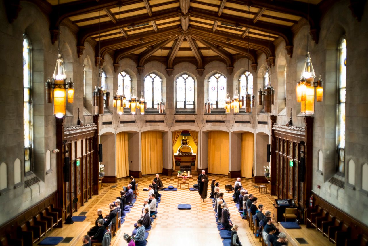 Elegant university dining hall with vaulted wooden ceiling, gothic windows, and pendant lights illuminating rows of tables.