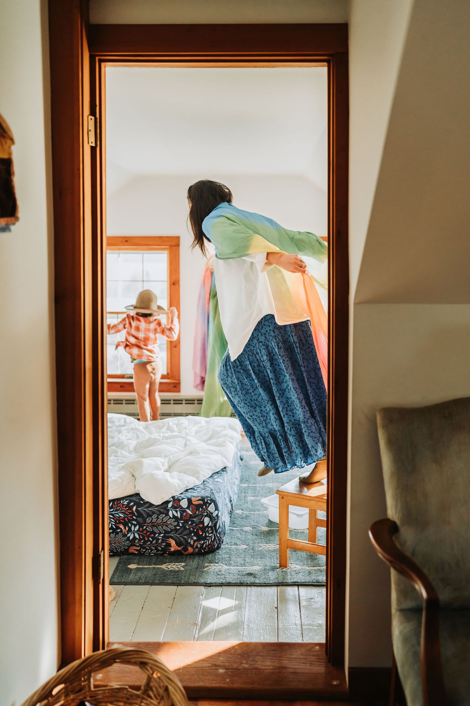 Through a doorway showing people in a light-filled room with scattered laundry and clothes strewn about the floor.