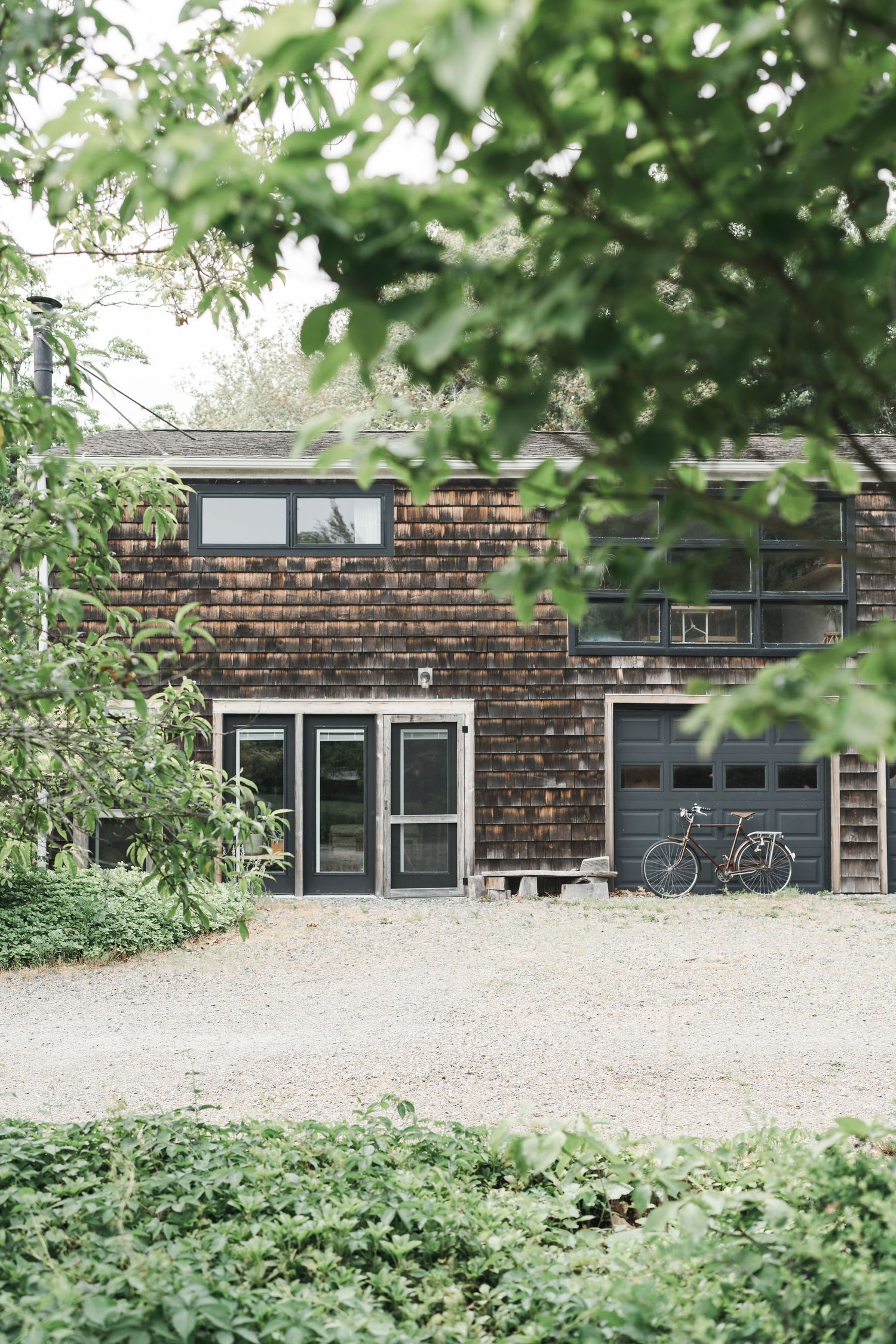Rustic brick building with modern windows and a bicycle parked outside, surrounded by lush greenery.