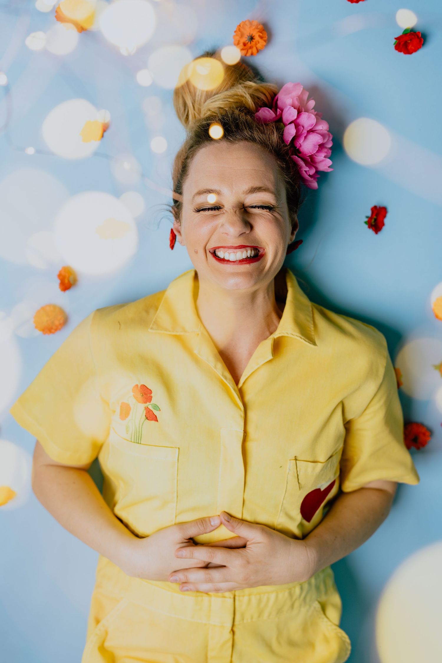Playful portrait with flowers and confetti against blue background.