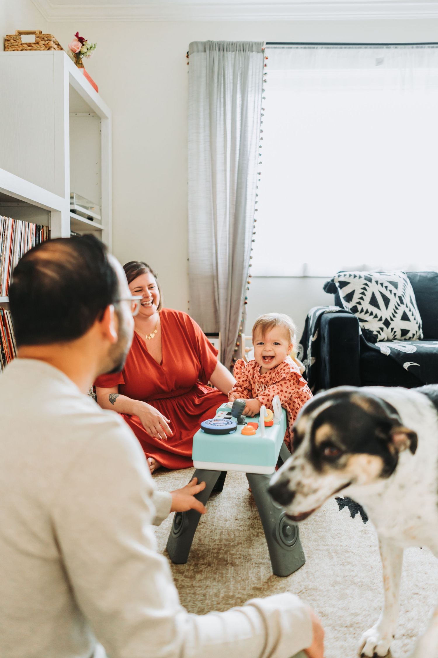 A family sits together on the floor of a cozy living room with their dog while sharing a moment at home.