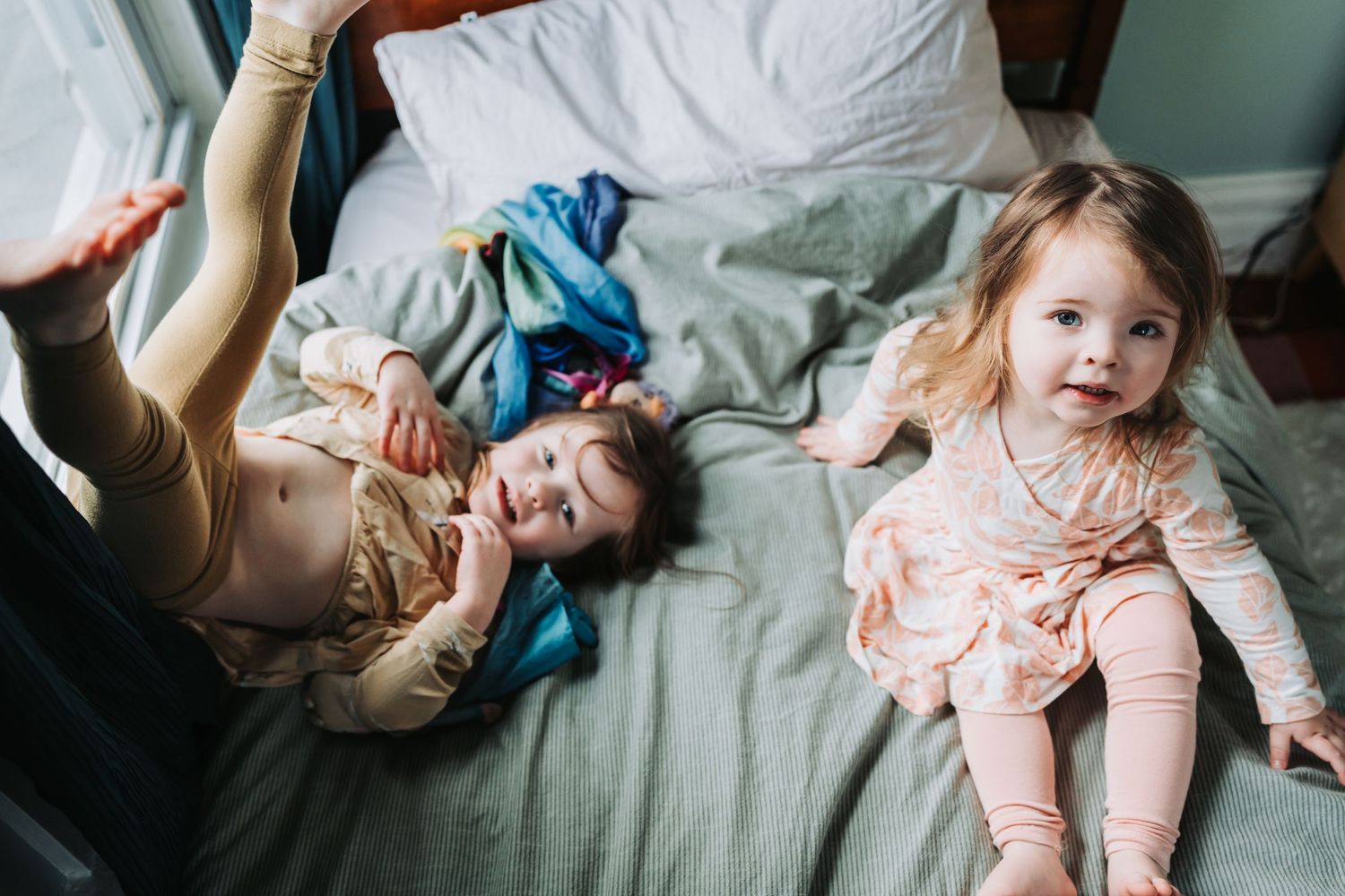 Joyful playtime on rumpled bed sheets with soft natural lighting.