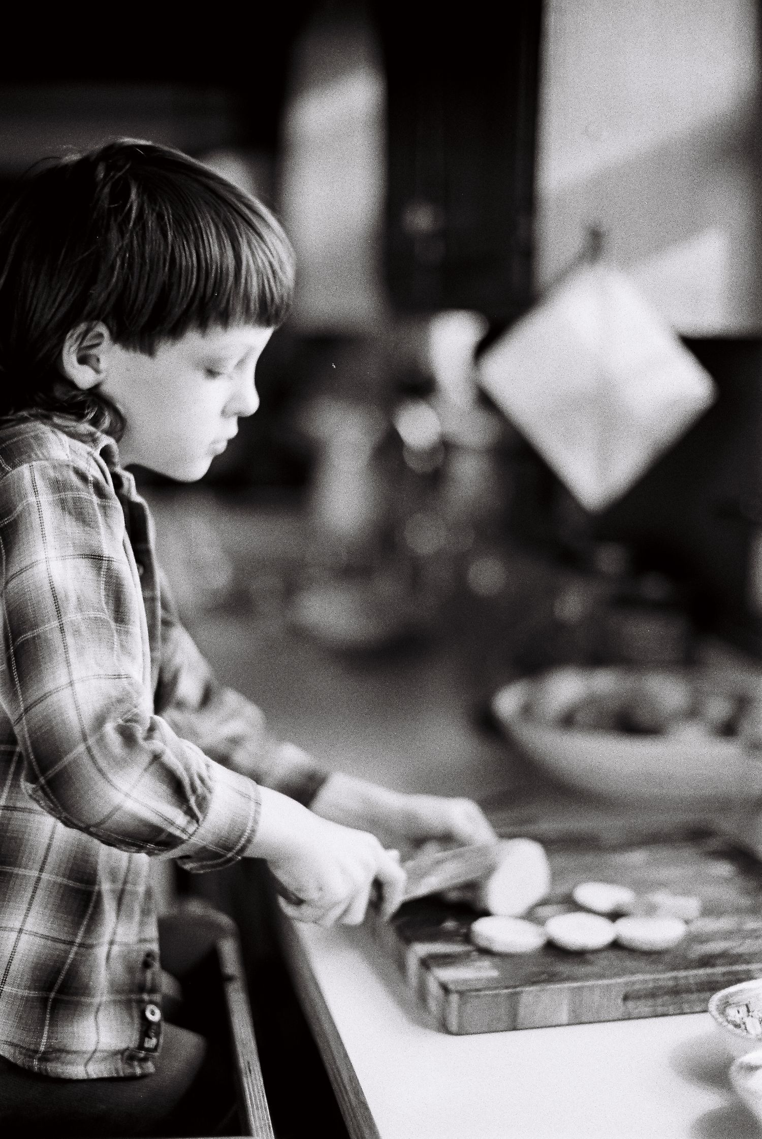 Black and white photo series showing a young child in a plaid shirt mixing and rolling dough in a kitchen.
