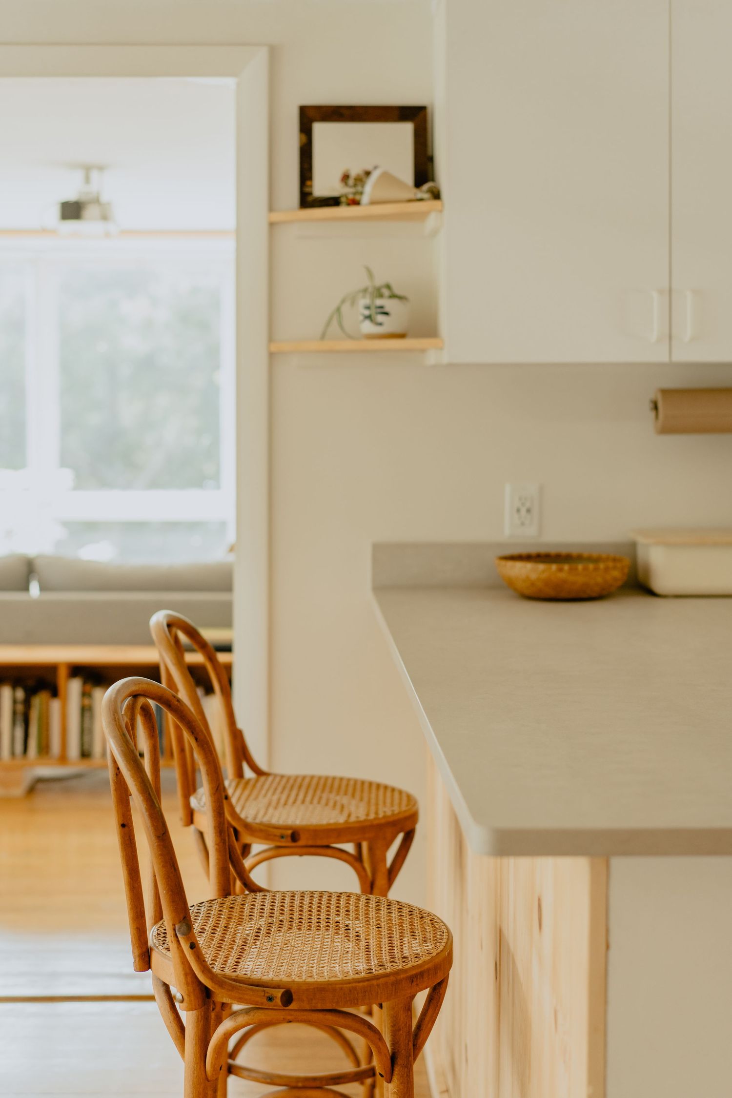 Three wooden bar stools with woven cane seats sit against a clean white kitchen counter with natural lighting.