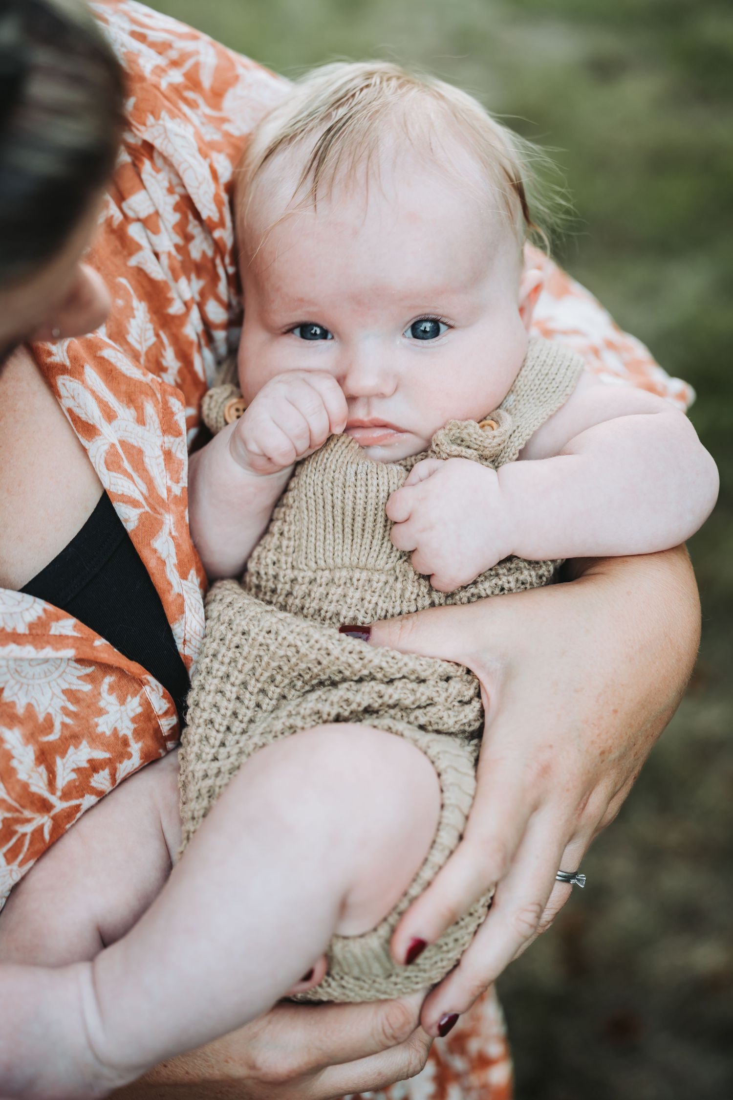 Baby in knit romper lying on floral print fabric while being gently held.